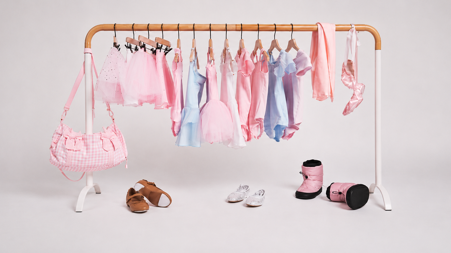 Pastel girls’ dancewear and ballet accessories displayed on a clothing rack, including leotards, tutus, ballet shoes, a dance bag, and warm-up booties.