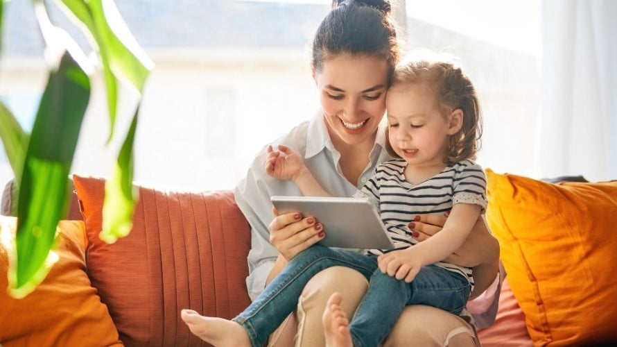 ChatGPT said: Mother and daughter sitting on a couch, smiling and looking at a tablet together.