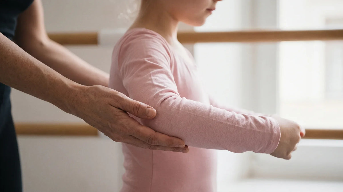 Ballet teacher gently guiding a young dancer's arm into a rounded position during port de bras practice