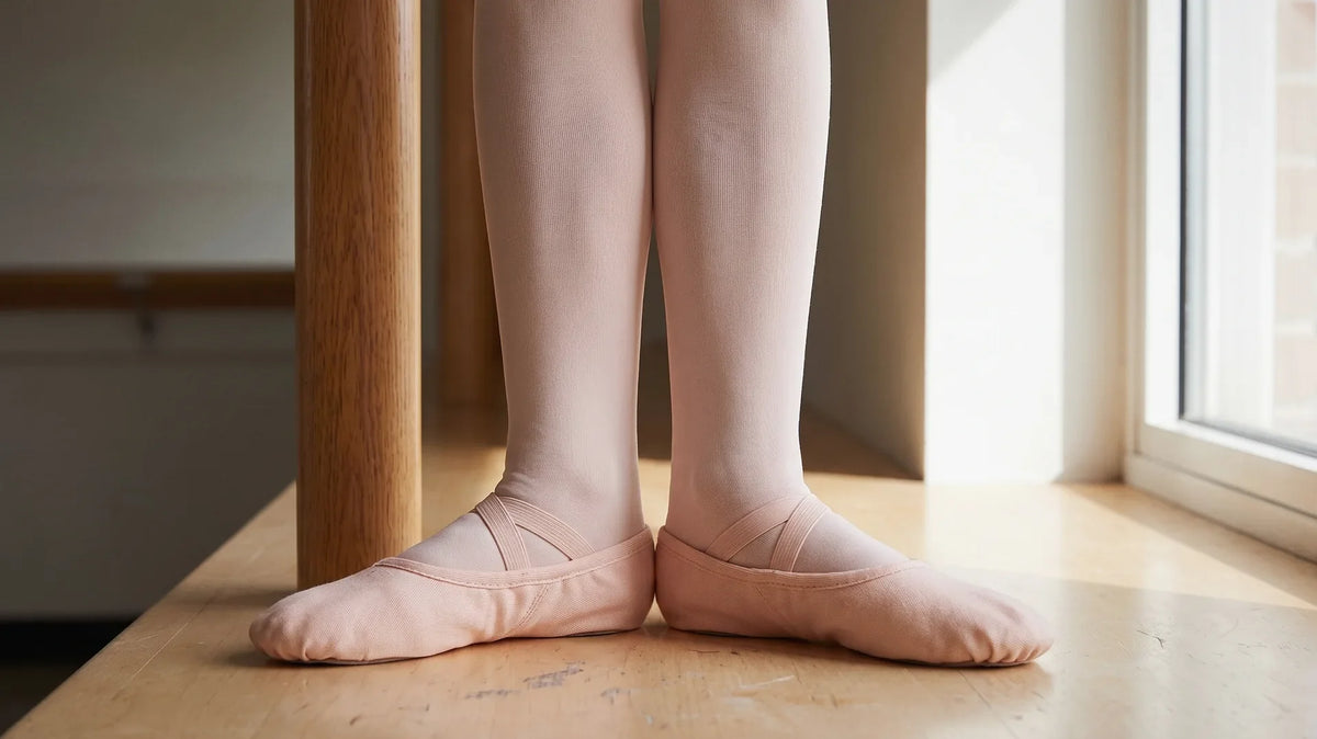 Young dancer's feet in ballet slippers turned out in first position beside the barre on a studio floor