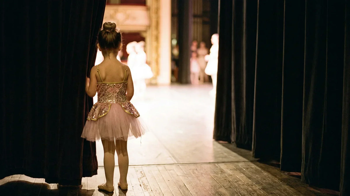 Young dancer in a recital costume waiting in the theater wings in warm stage light, seen from behind