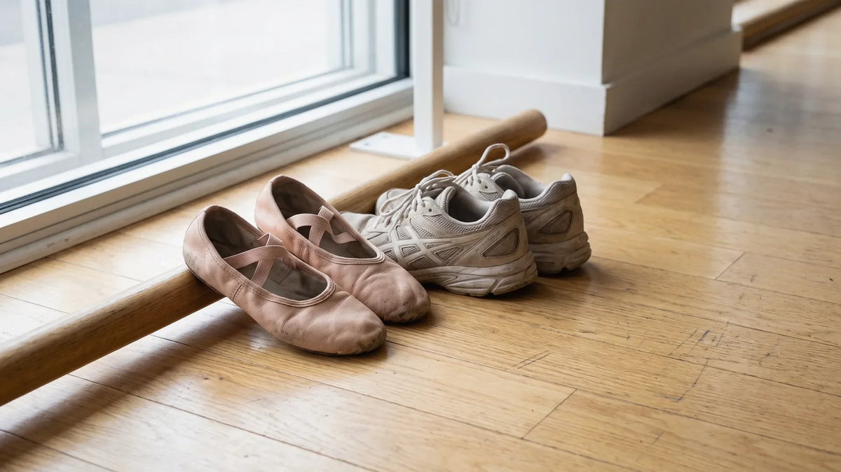 Worn pink ballet shoes next to athletic sneakers on a studio floor, asking whether ballet is a sport
