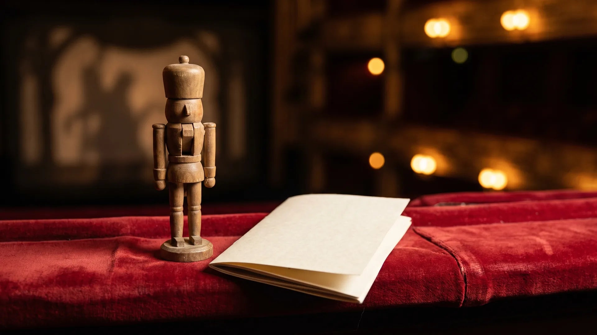 Wooden nutcracker doll on a red velvet theater seat beside a program