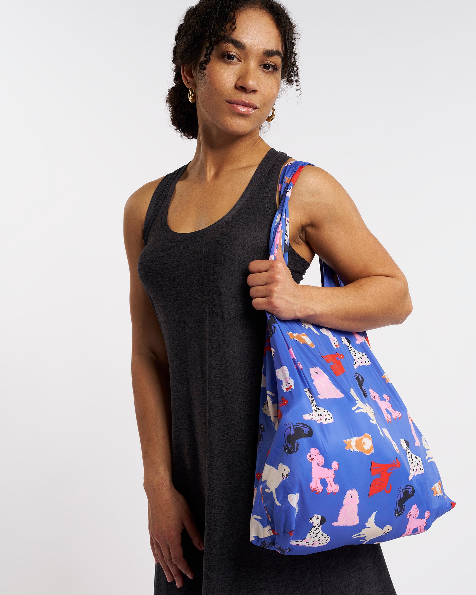 Model carrying Puppy Parade on Blue Stelle reusable grocery bag with puppy print over the shoulder, a lightweight foldable bag for markets and errands.