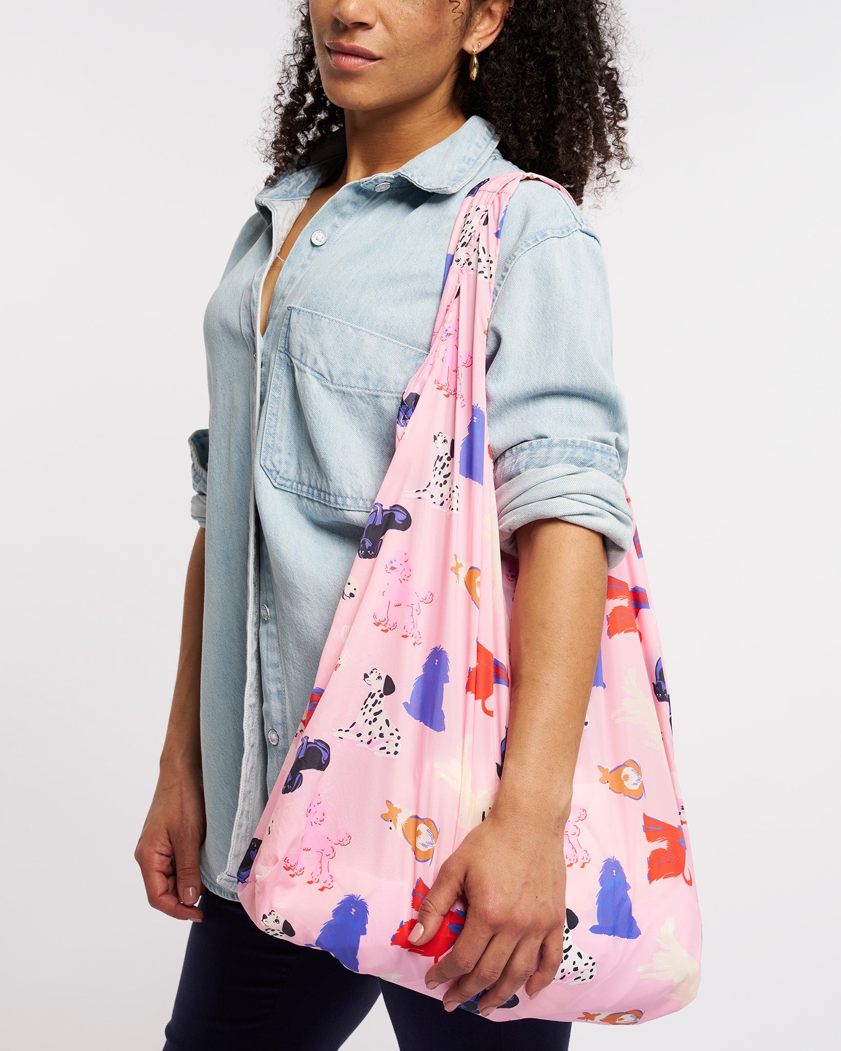 Model carrying Puppy Parade on Pink Stelle reusable grocery bag with puppy print over the shoulder, a lightweight foldable bag for markets and errands.