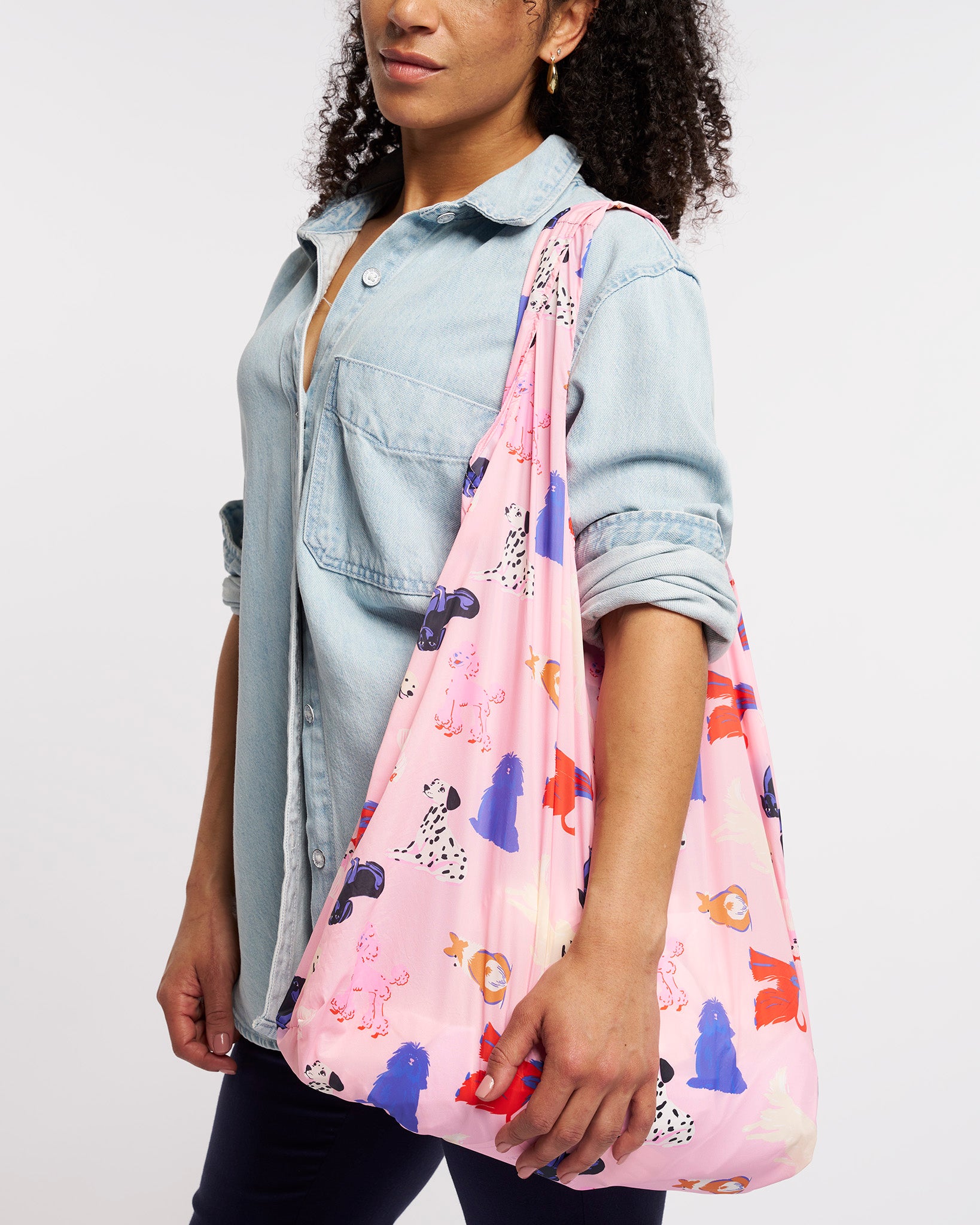 Model carrying Puppy Parade on Pink Stelle reusable grocery bag with puppy print over the shoulder, a lightweight foldable bag for markets and errands.