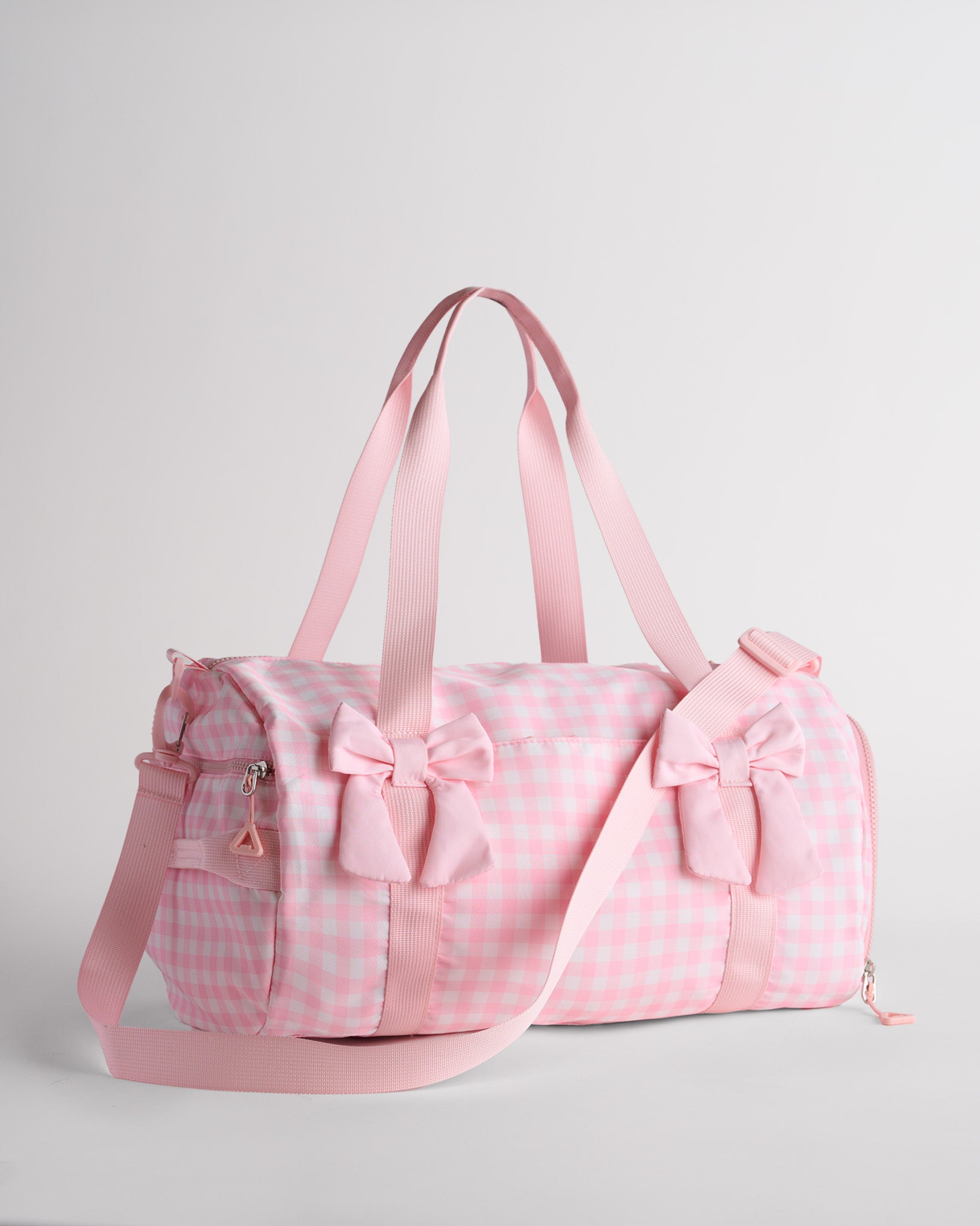 Pink gingham kids duffle bag with bow details, top handles and adjustable shoulder strap for dance and travel.