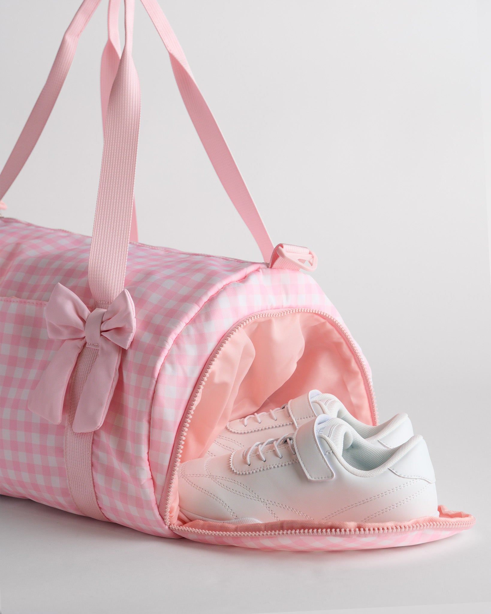 Kids pink gingham duffle bag with side shoe compartment holding sneakers, ideal for separating shoes from clothes.
