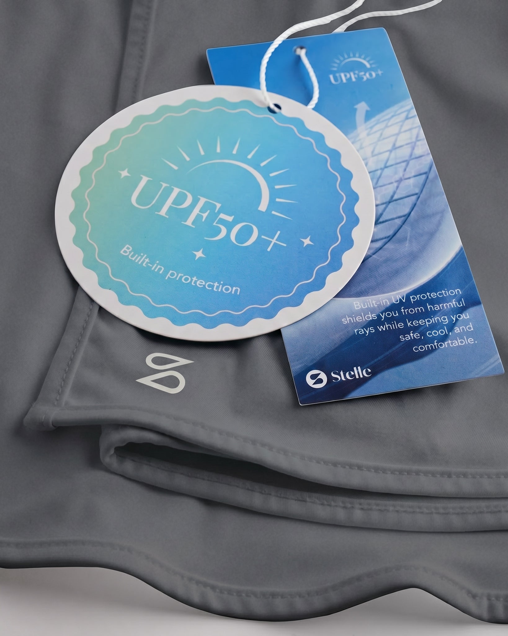 Close-up of grey sunscreen face mask showing UPF 50+ built-in protection tag, smooth fabric, and Stelle logo.