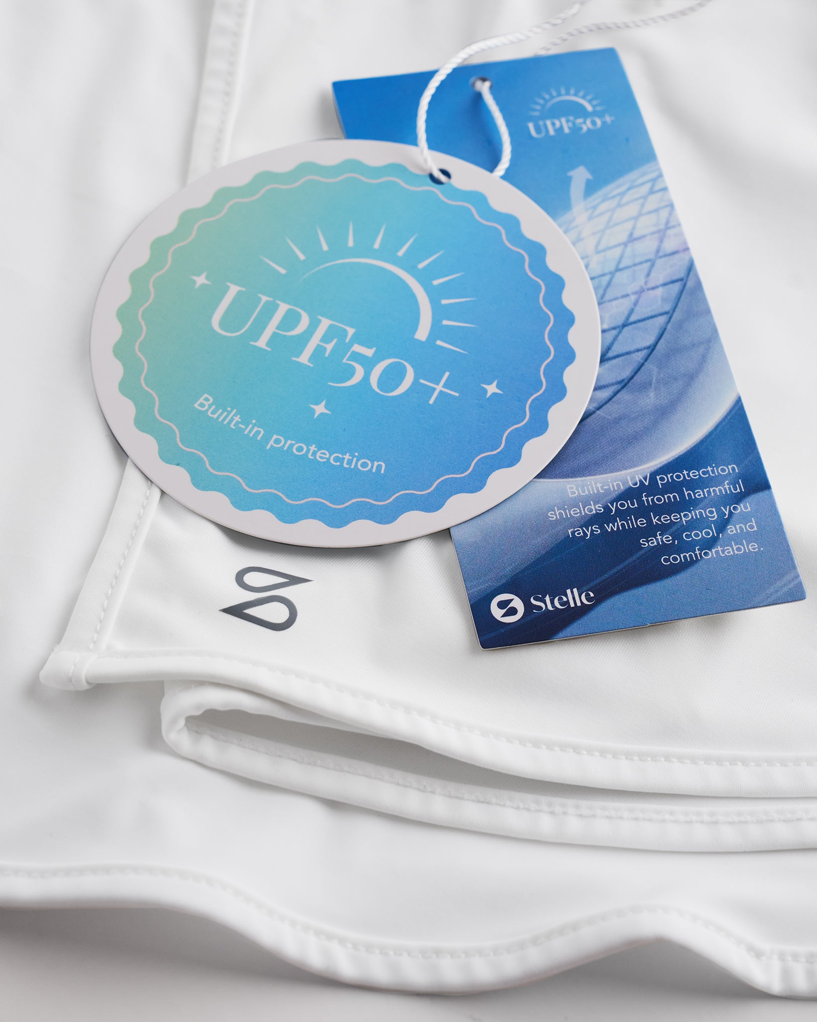 Close-up of white sunscreen face mask showing UPF 50+ built-in protection tag, smooth fabric, and Stelle logo.