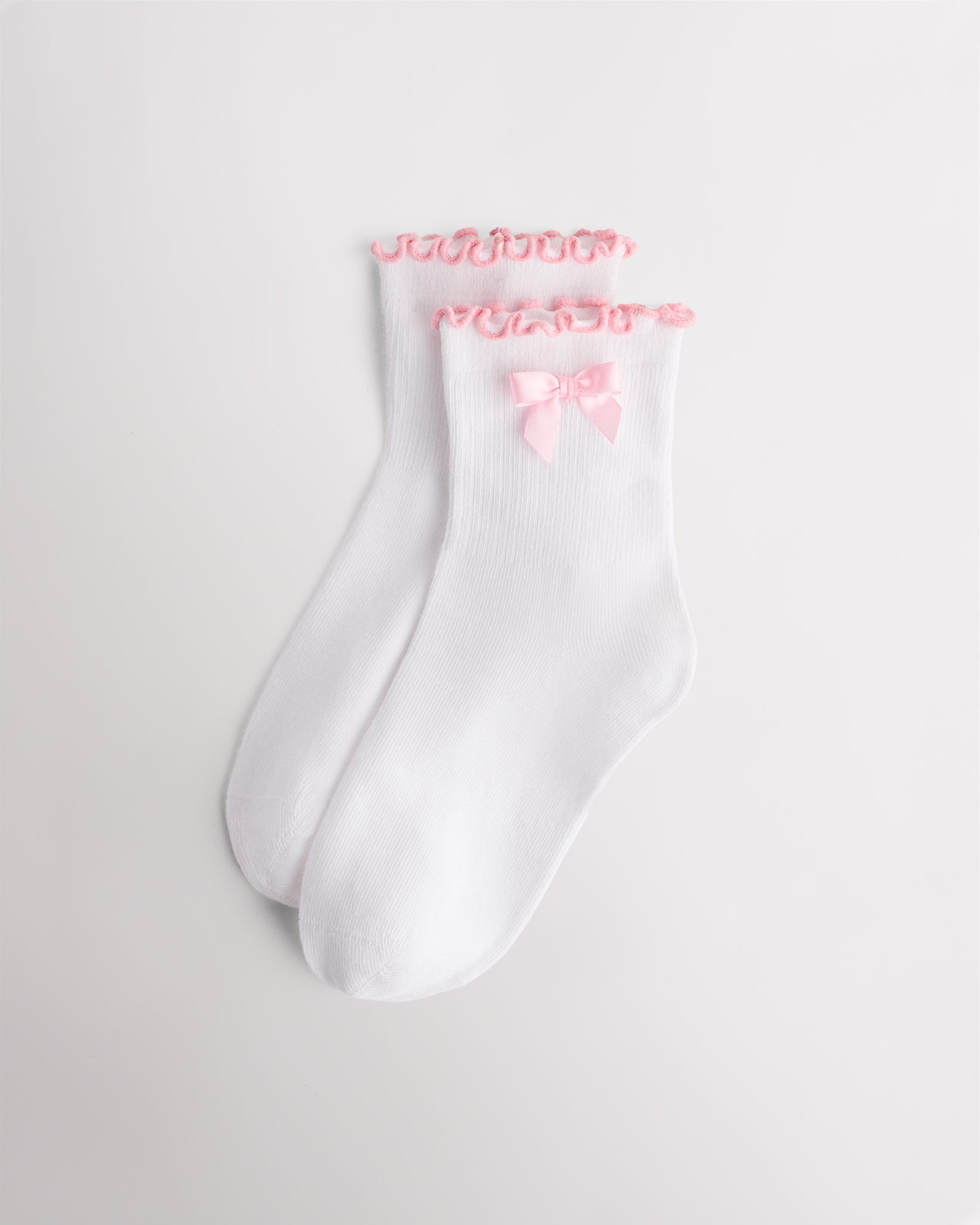 White kids socks with pink ribbon bow, pink lettuce-edge ruffle cuffs, and ribbed texture