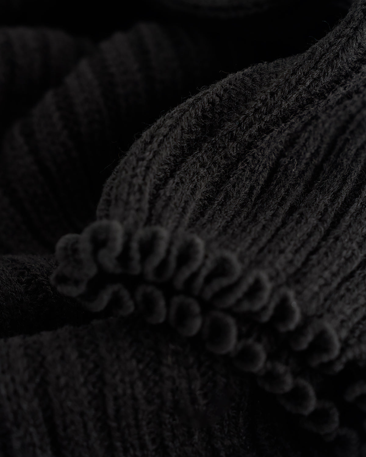 Close-up of black ballet leg warmers showing soft knit texture and delicate lettuce-edge trim.