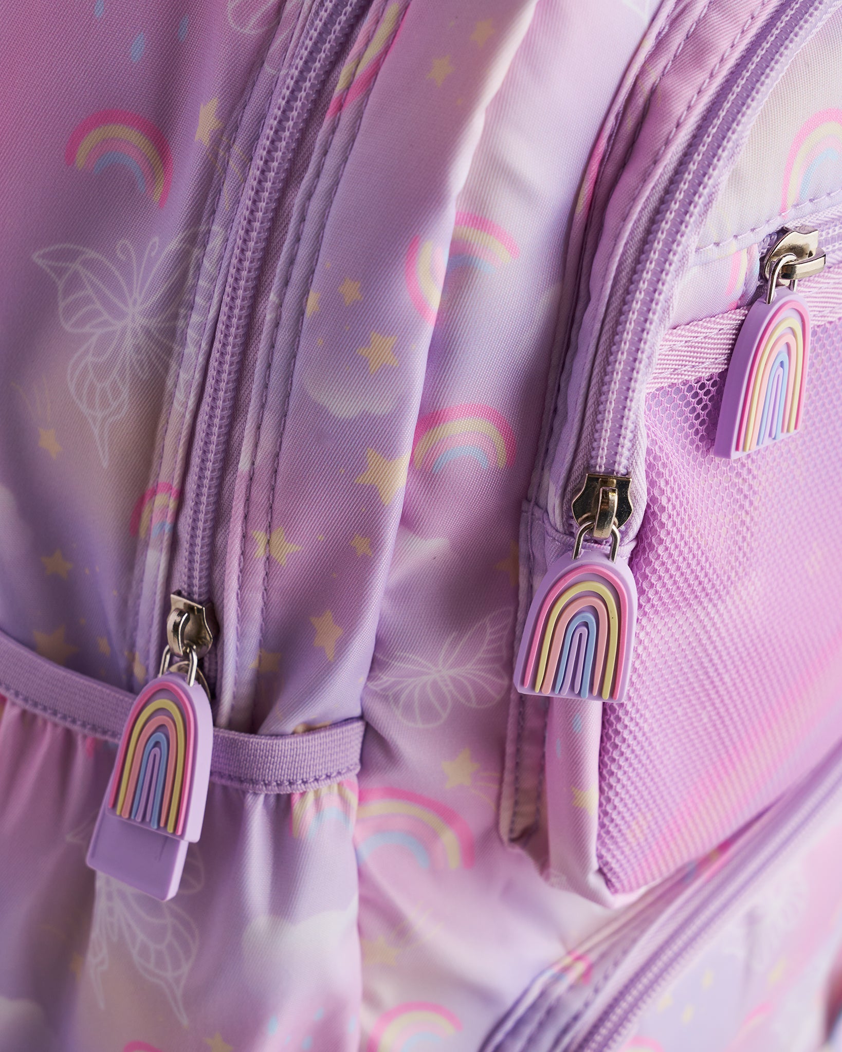 Close-up of lavender Stelle kids backpack showing rainbow zipper pulls, mesh pocket, and pastel rainbow print.