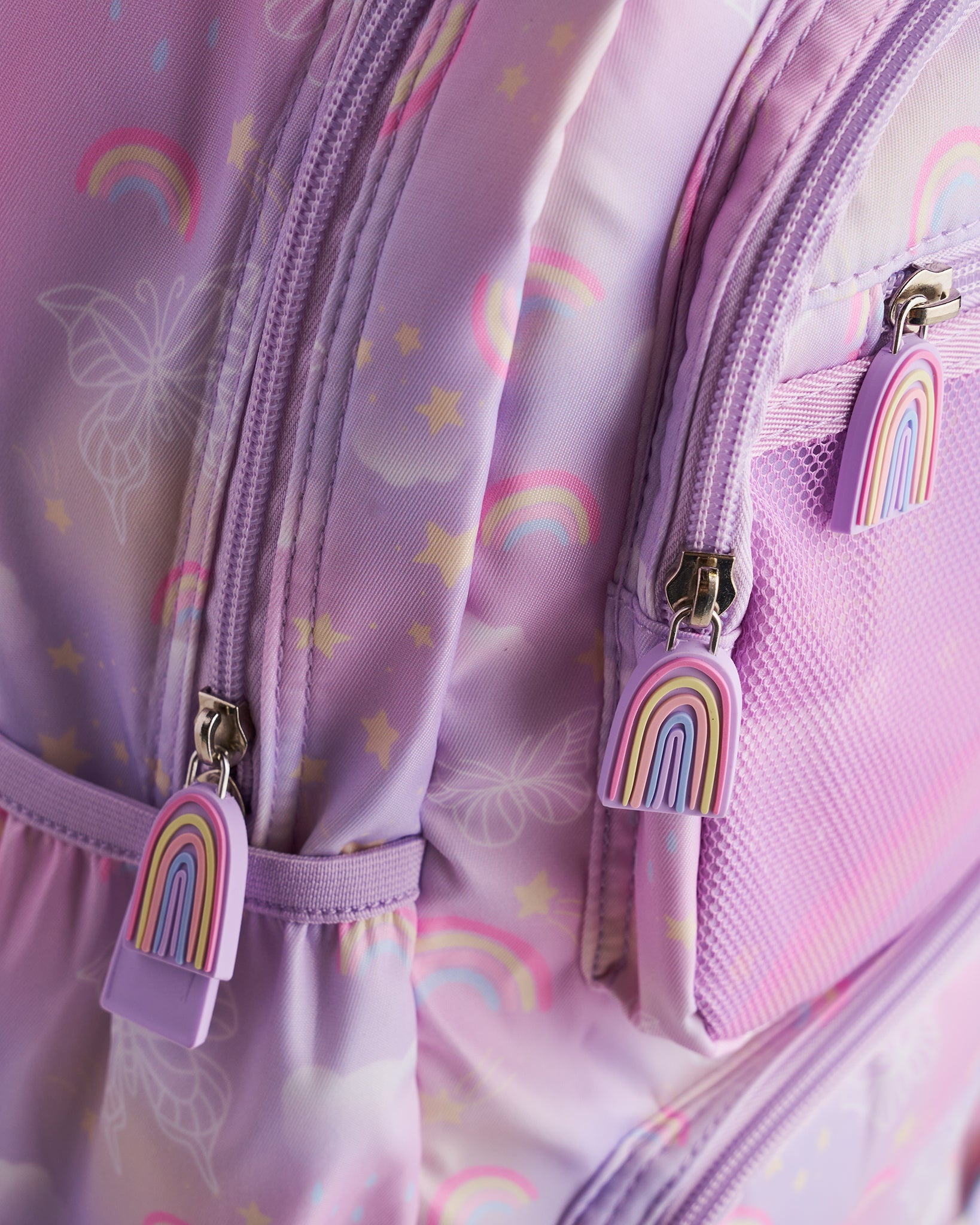 Close-up of lavender Stelle kids backpack showing rainbow zipper pulls, mesh pocket, and pastel rainbow print.