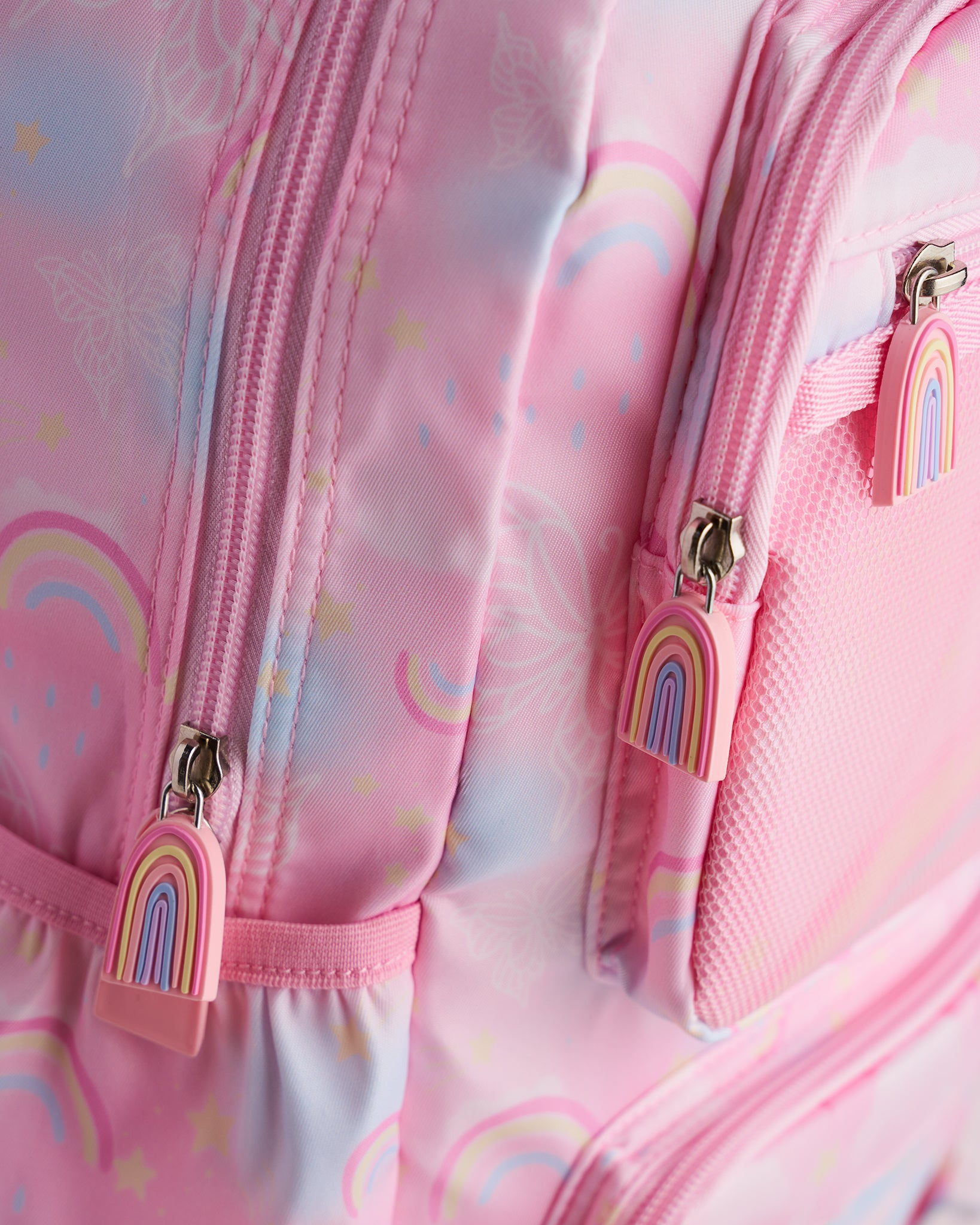 Close-up of pink kids backpack showing rainbow zipper pulls, front mesh pocket, and pastel rainbow print.