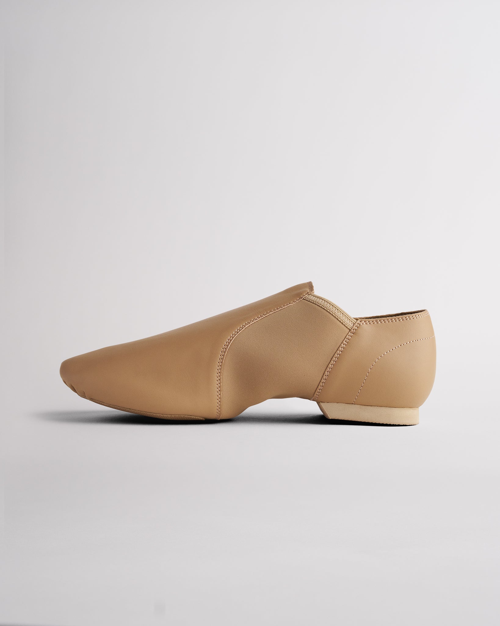 Side view of tan vegan leather jazz shoe showing slip-on design, stitched details, and flexible dance shoe shape.