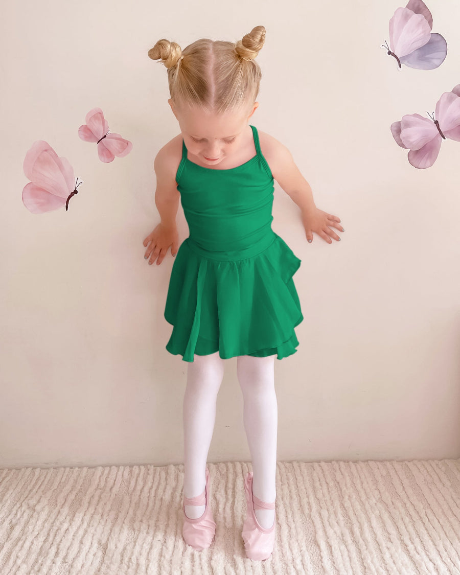 Young girl in a green dress standing against a light pink wall with butterfly decorations.