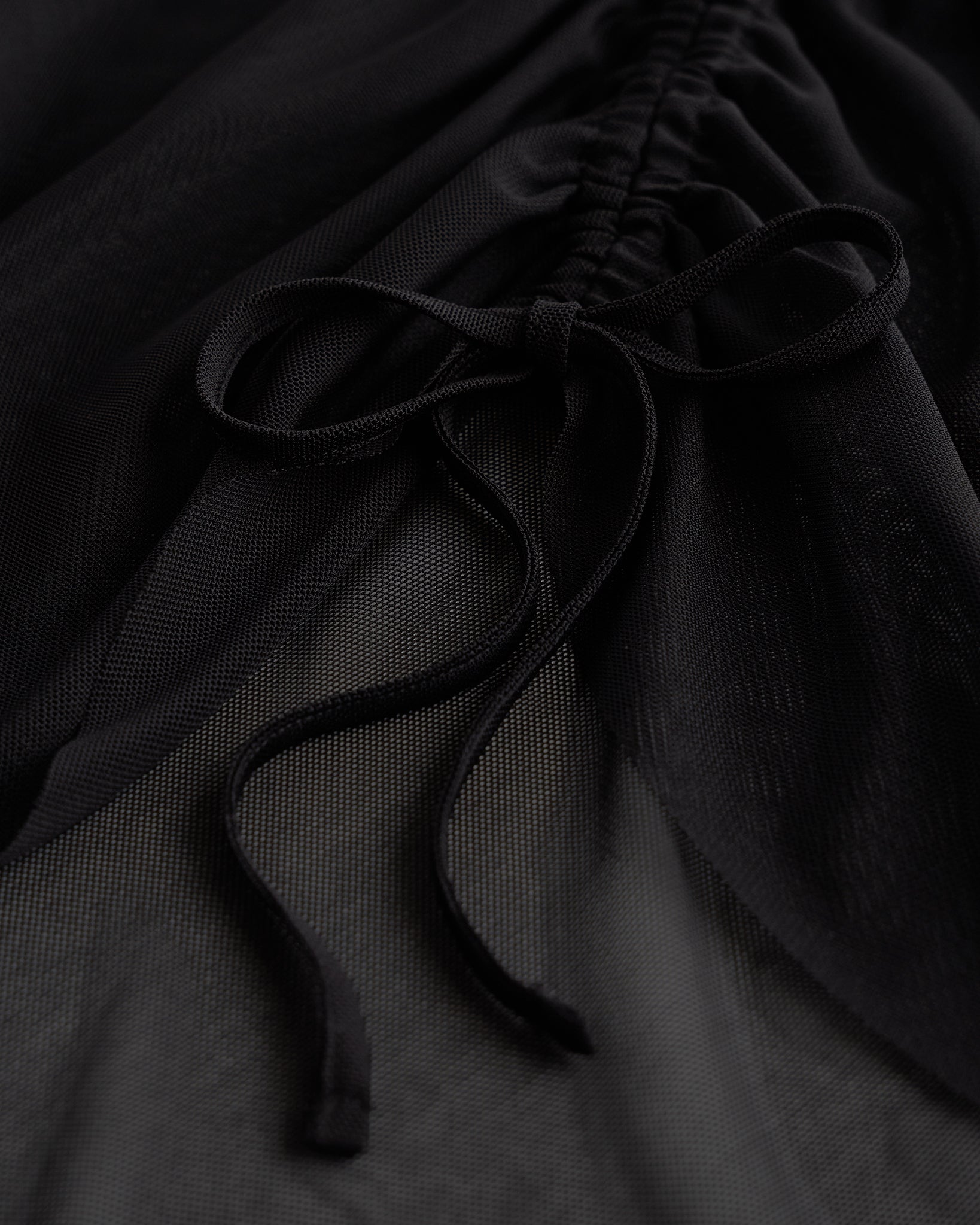 Close-up of black mesh ballet skirt showing adjustable ruched drawstring and soft sheer fabric.