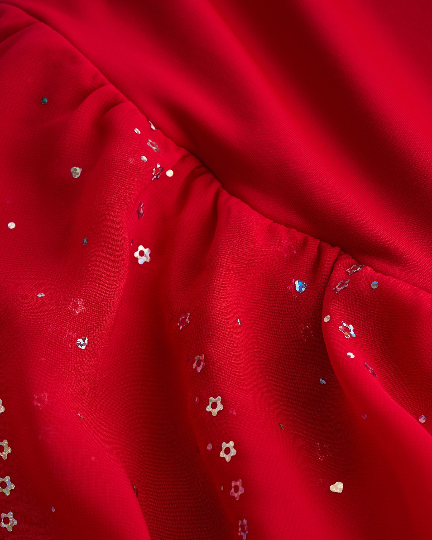 Close-up of red dance dress fabric with sparkling floral sequins on chiffon for a playful ballet performance look.