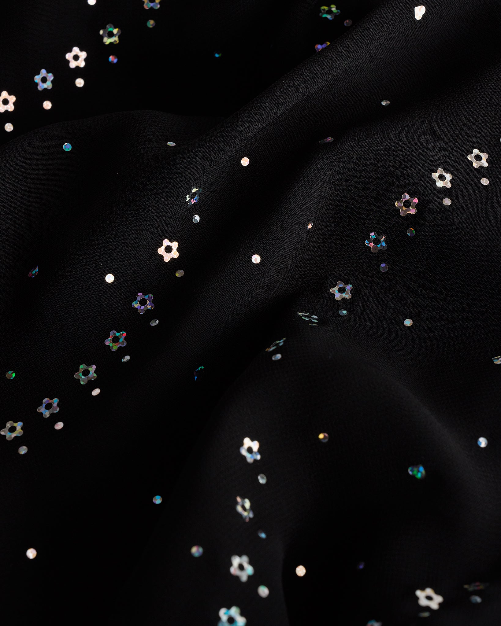 Close-up of black dance dress fabric with sparkling floral sequins on chiffon for a playful ballet performance look.