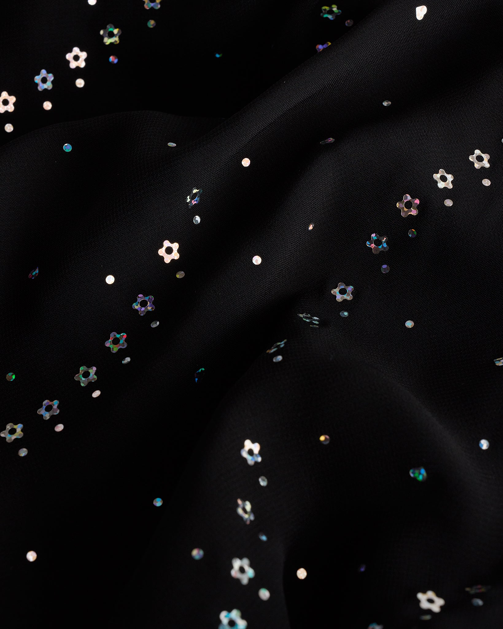 Close-up of black dance dress fabric with sparkling floral sequins on chiffon for a playful ballet performance look.