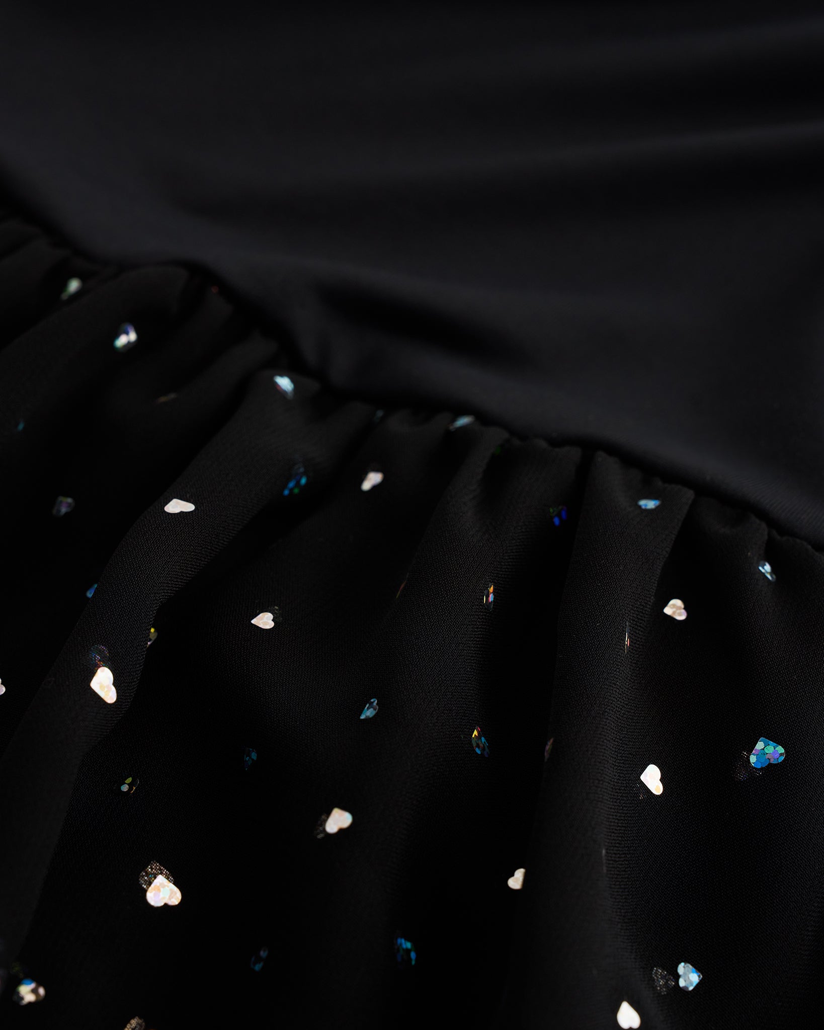 Close-up of black sequin dress showing heart-shaped sequins, chiffon skirt fabric, and gathered waist detail.