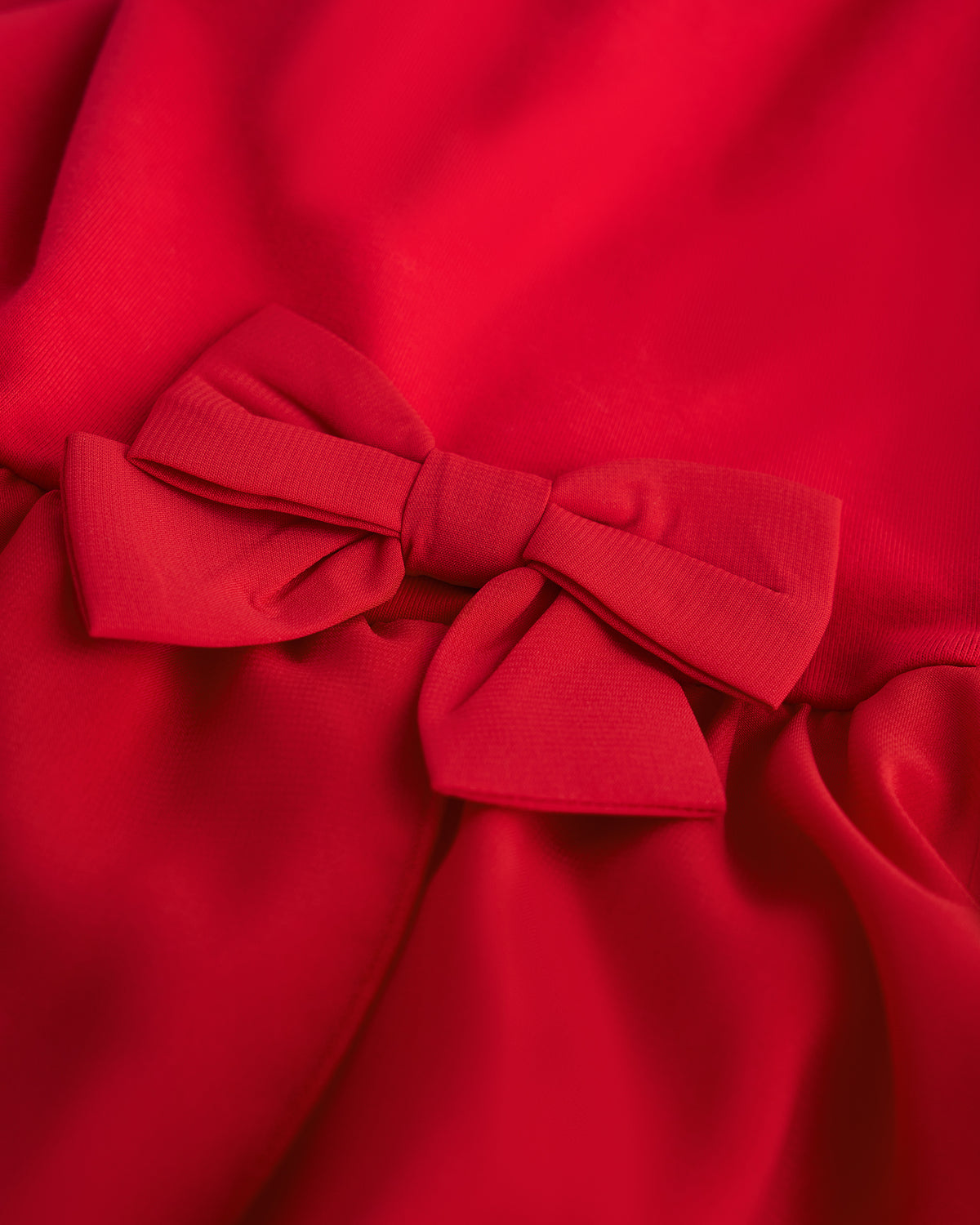 Close-up of red ballet dress showing the decorative bow accent and soft chiffon wrap skirt.