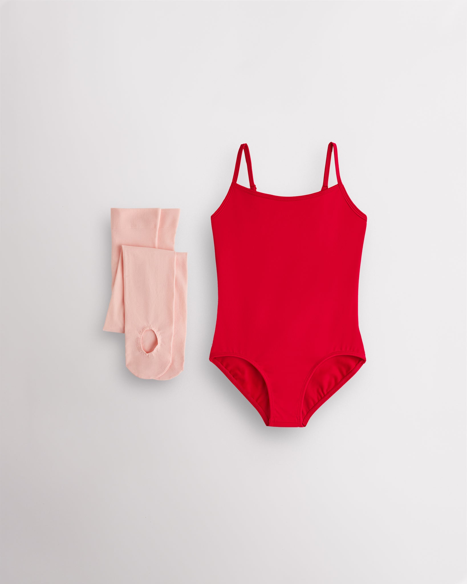 Red girls camisole leotard with pink convertible dance tights laid flat for ballet and dance class.