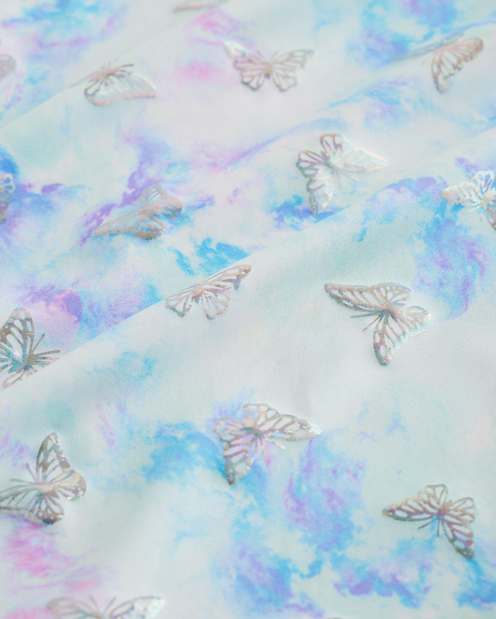 Close-up of Butterfly Mist girls unitard fabric showing butterflies, rainbows, moons, stars, and soft shimmer detail.