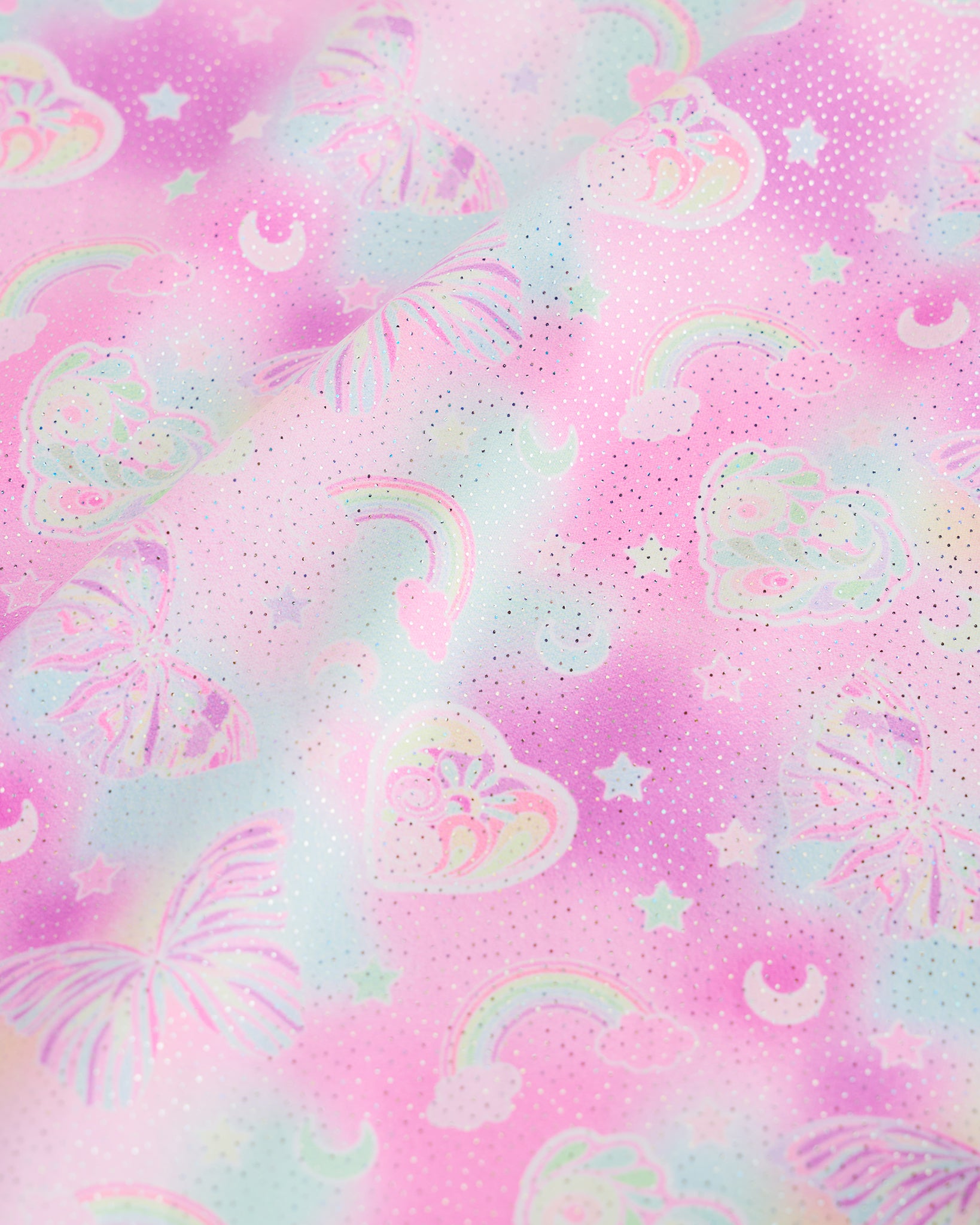 Close-up of Bow Dreams girls unitard fabric showing butterflies, rainbows, moons, stars, and soft shimmer detail.