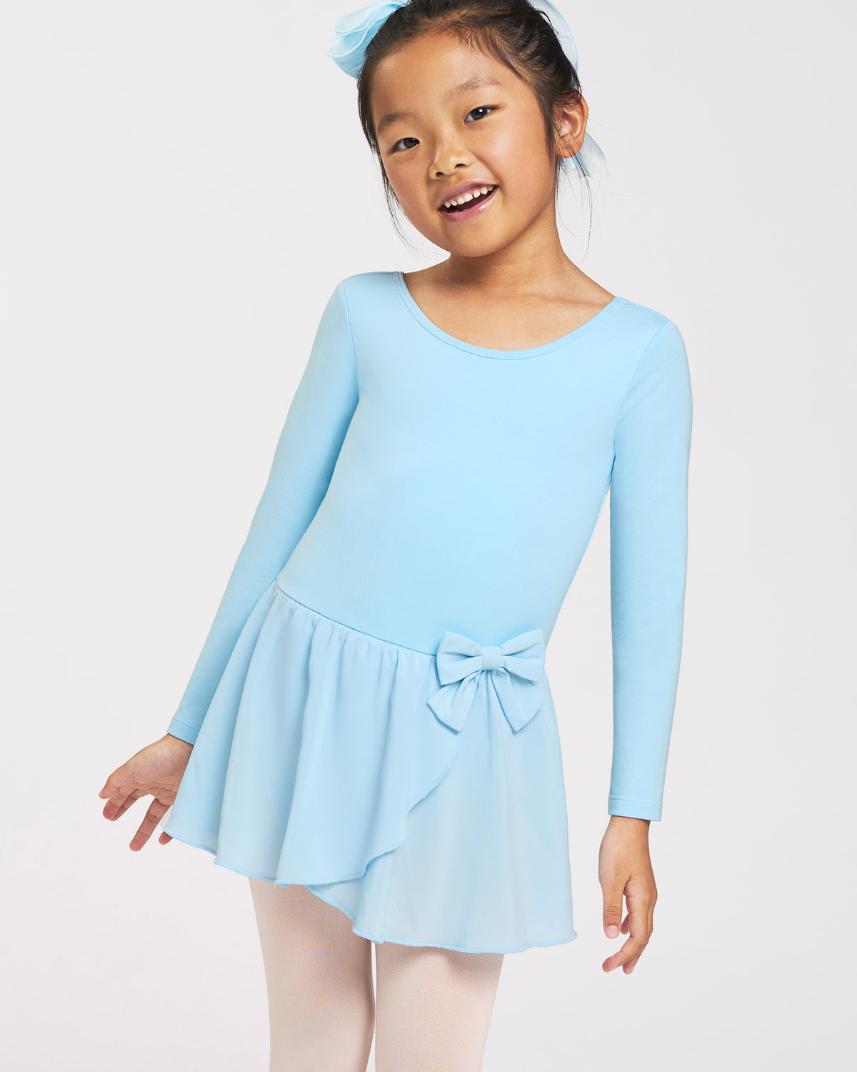 Girl wearing a blue long sleeve ballet dress with crew neckline, attached chiffon wrap skirt, bow accent, and ballet tights.