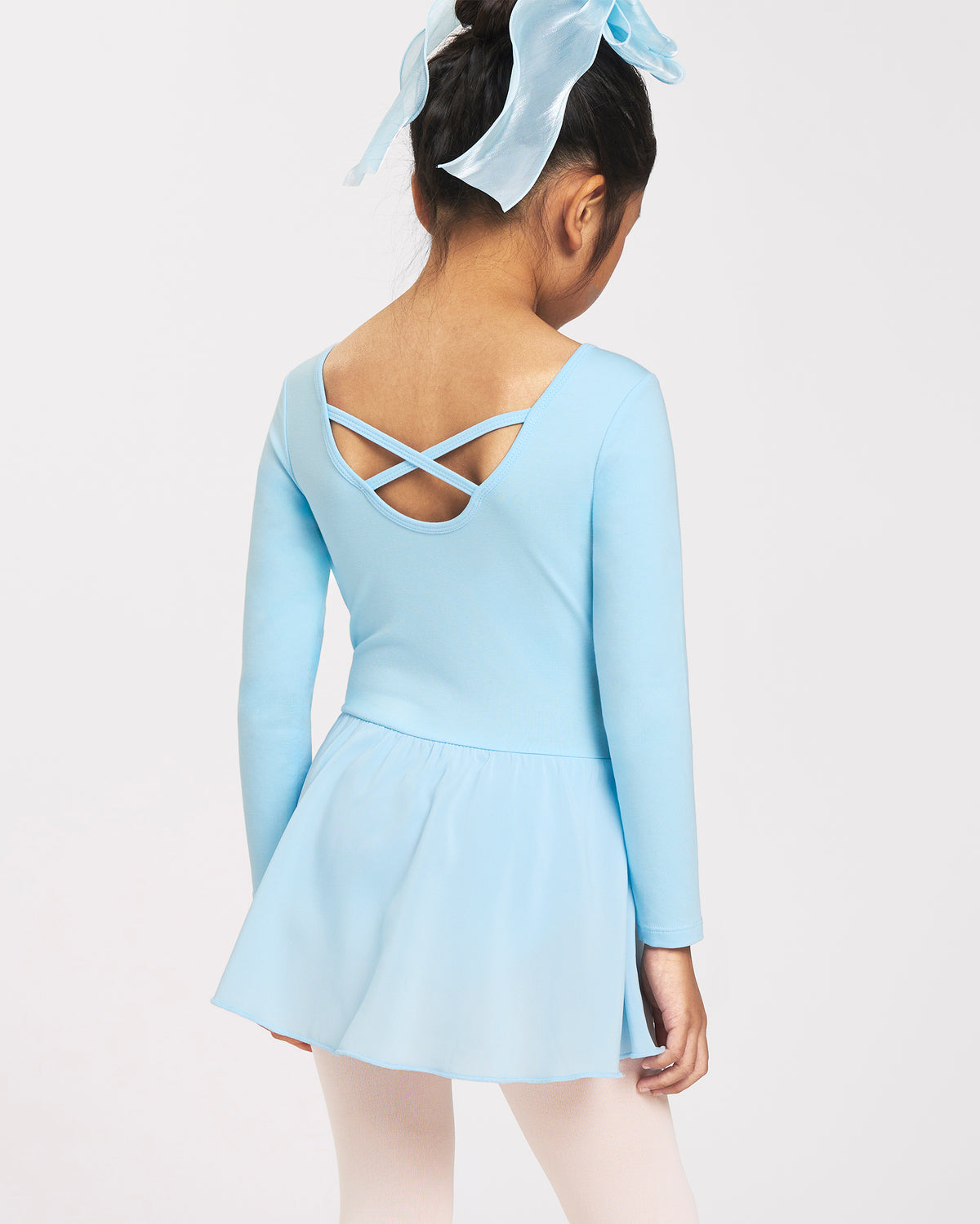 Back view of girl wearing a blue ballerina dress with long sleeves, crisscross back detail, chiffon skirt, and bow accent.