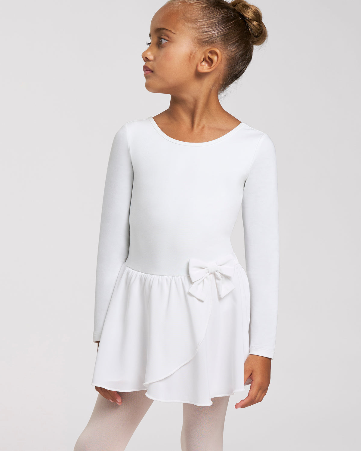 Girl wearing a white long sleeve ballet dress with crew neckline, attached chiffon wrap skirt, bow accent, and ballet tights.
