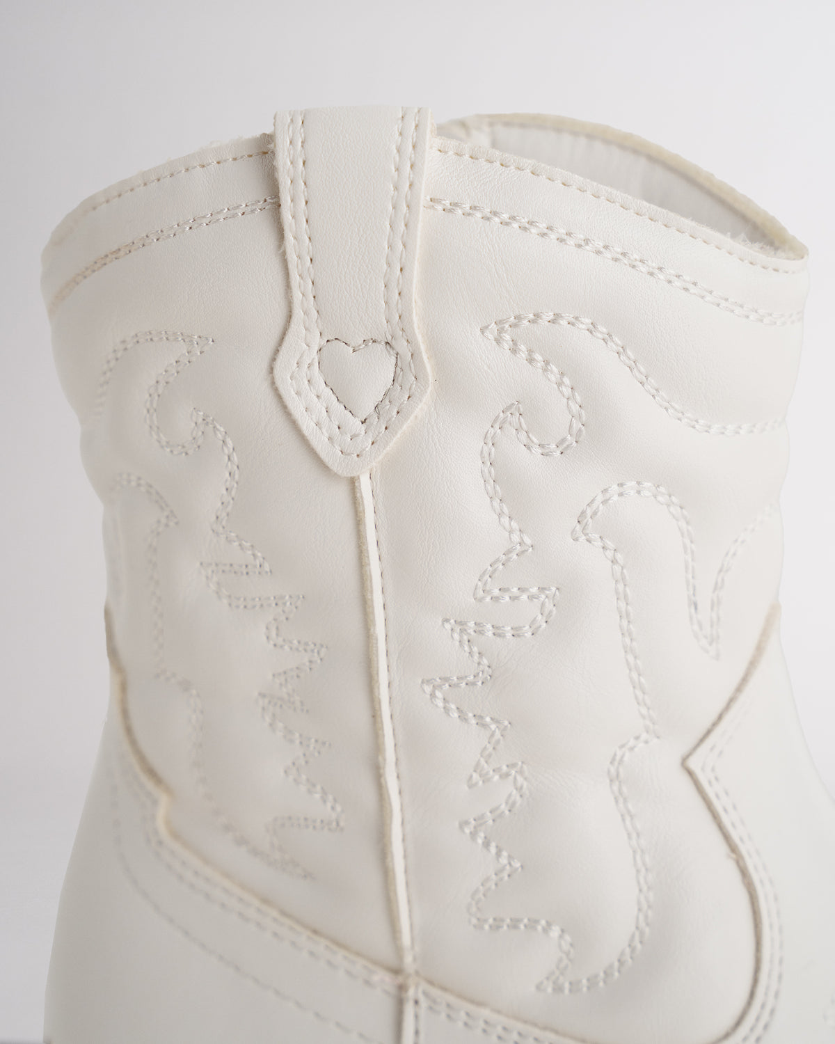 Close-up of the white cowboy boot pull tab with heart detail and tonal western stitching