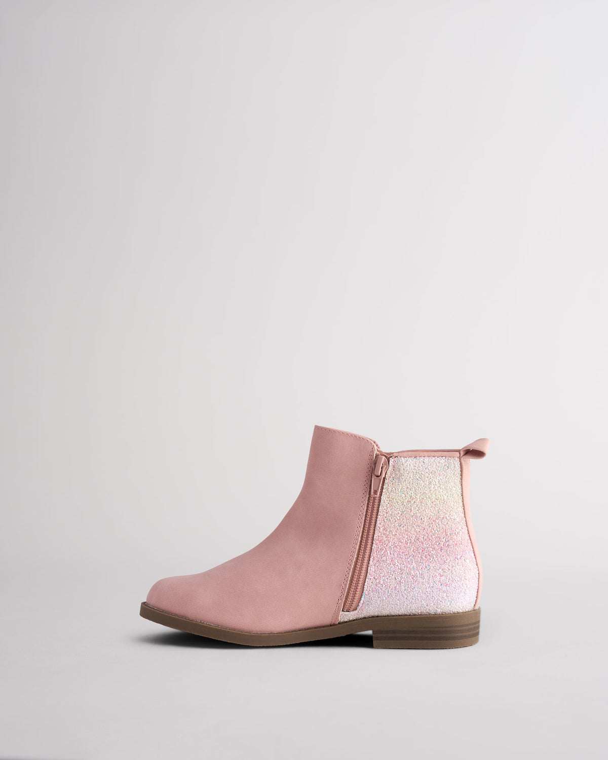 Side view of a kids pink faux suede ankle boot with a rainbow glitter heel and side zip, on a non-slip sole