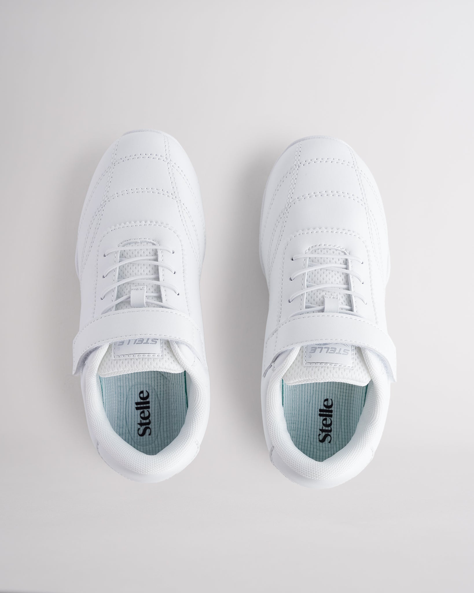 Top view of girls white cheer shoes with Velcro strap and lace design for secure fit.