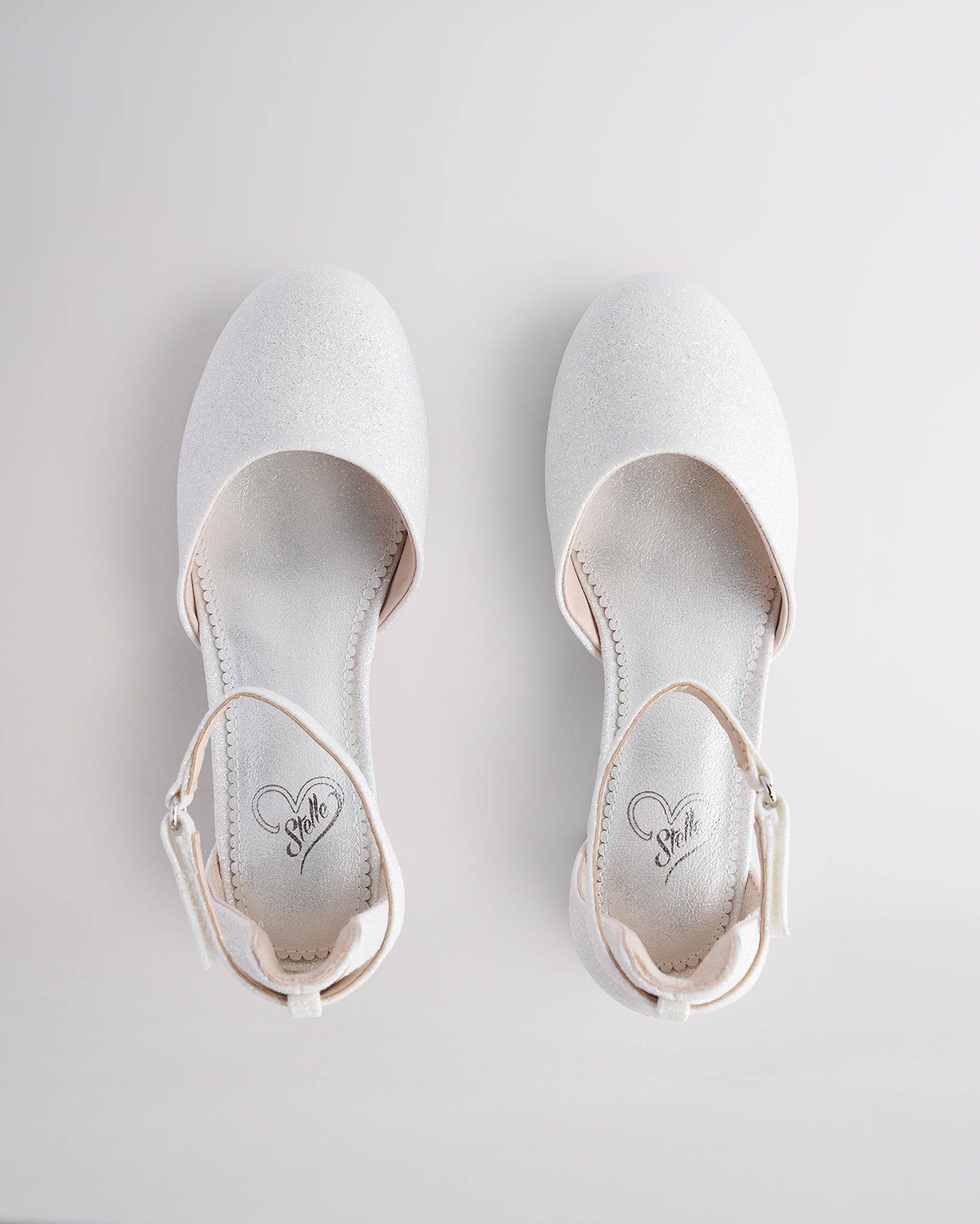 Girls’ white glitter dress shoes with a low block heel and ankle strap.