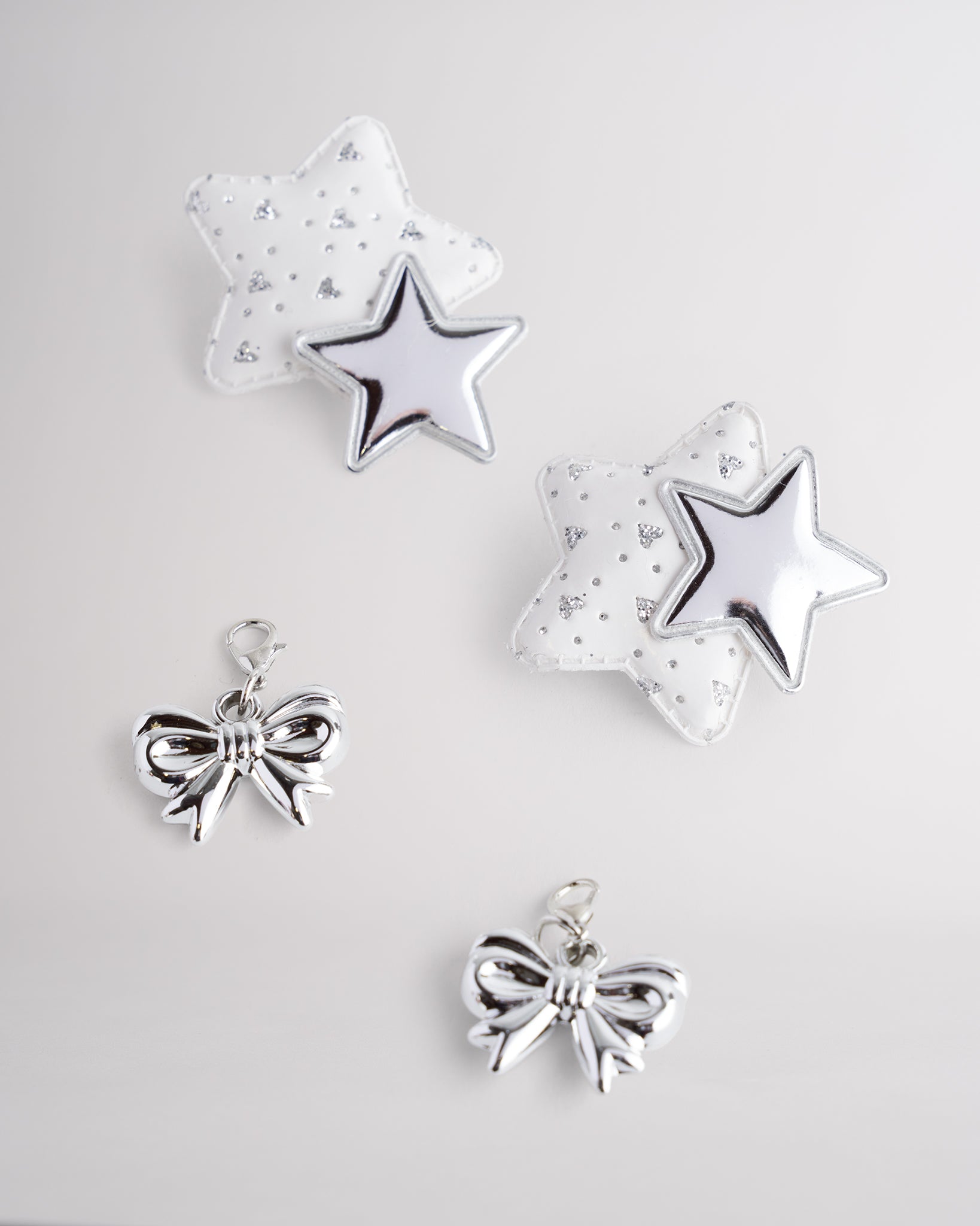 Silver bow and star shoe charms with glitter and metallic finishes shown on a white background.