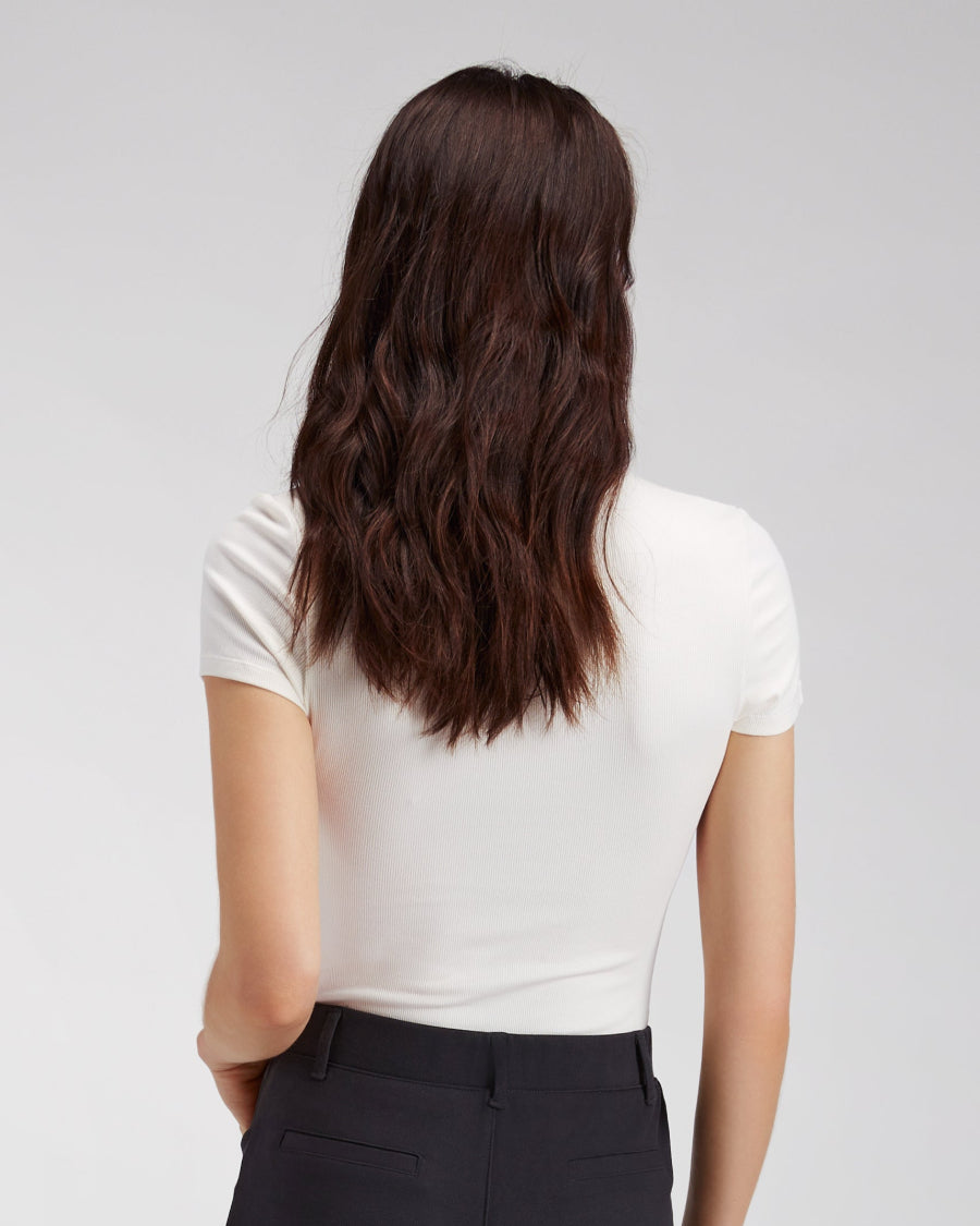 Person wearing a white shirt and black pants with long dark hair on a plain background