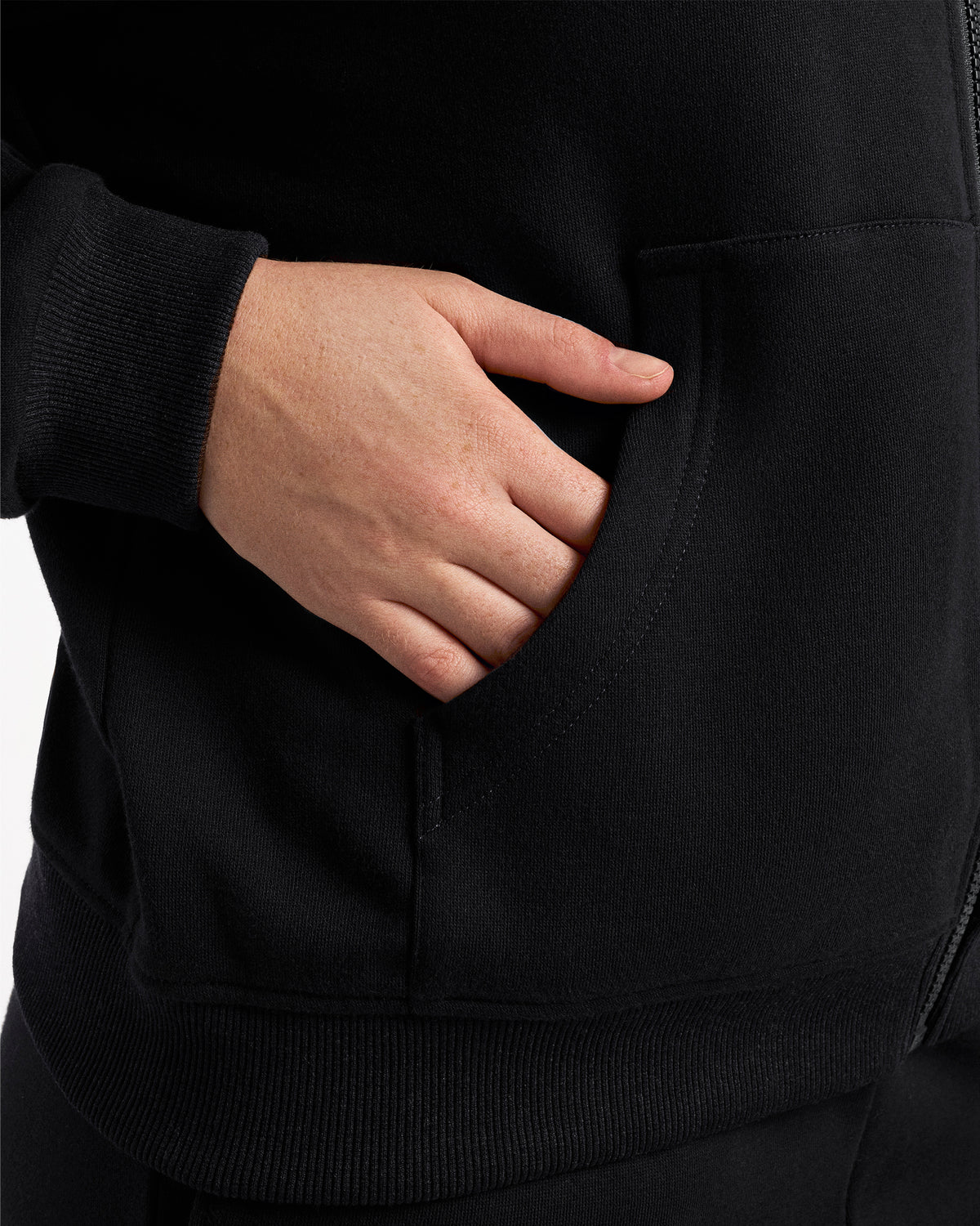 Close-up of a hand in the kangaroo pocket of the black fleece-lined zip-up hoodie.