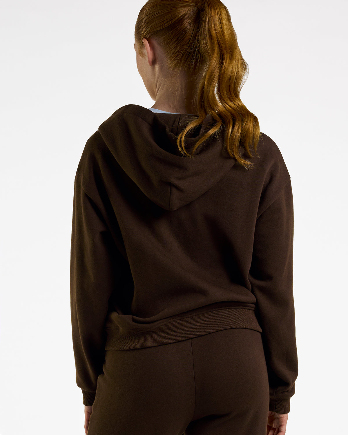Back view of a woman wearing the brown Coffee Stelle fleece-lined zip-up hoodie with the hood down.