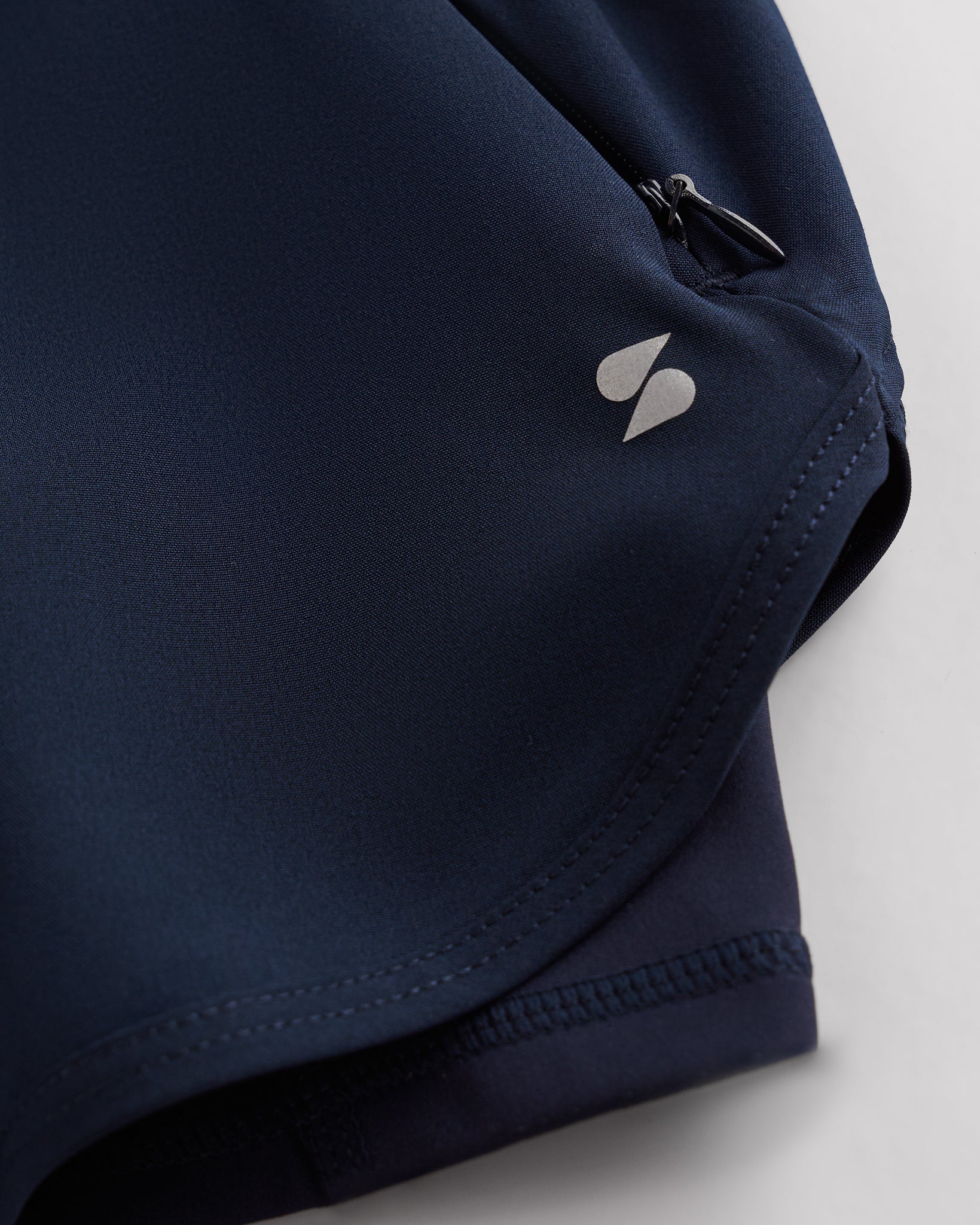 Close-up of navy Stelle gym shorts showing zipper pocket, curved hem stitching, and smooth performance fabric.