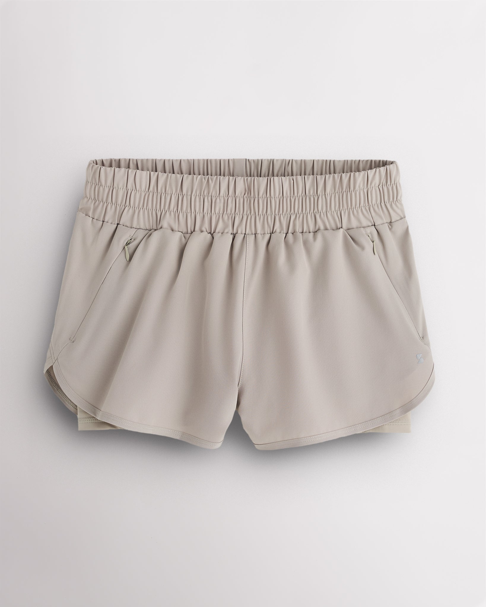 Sandy Grey Stelle RushMode 2-in-1 running shorts with wide elastic waistband, zipper pockets, inner shorts lining, and curved dolphin hem.