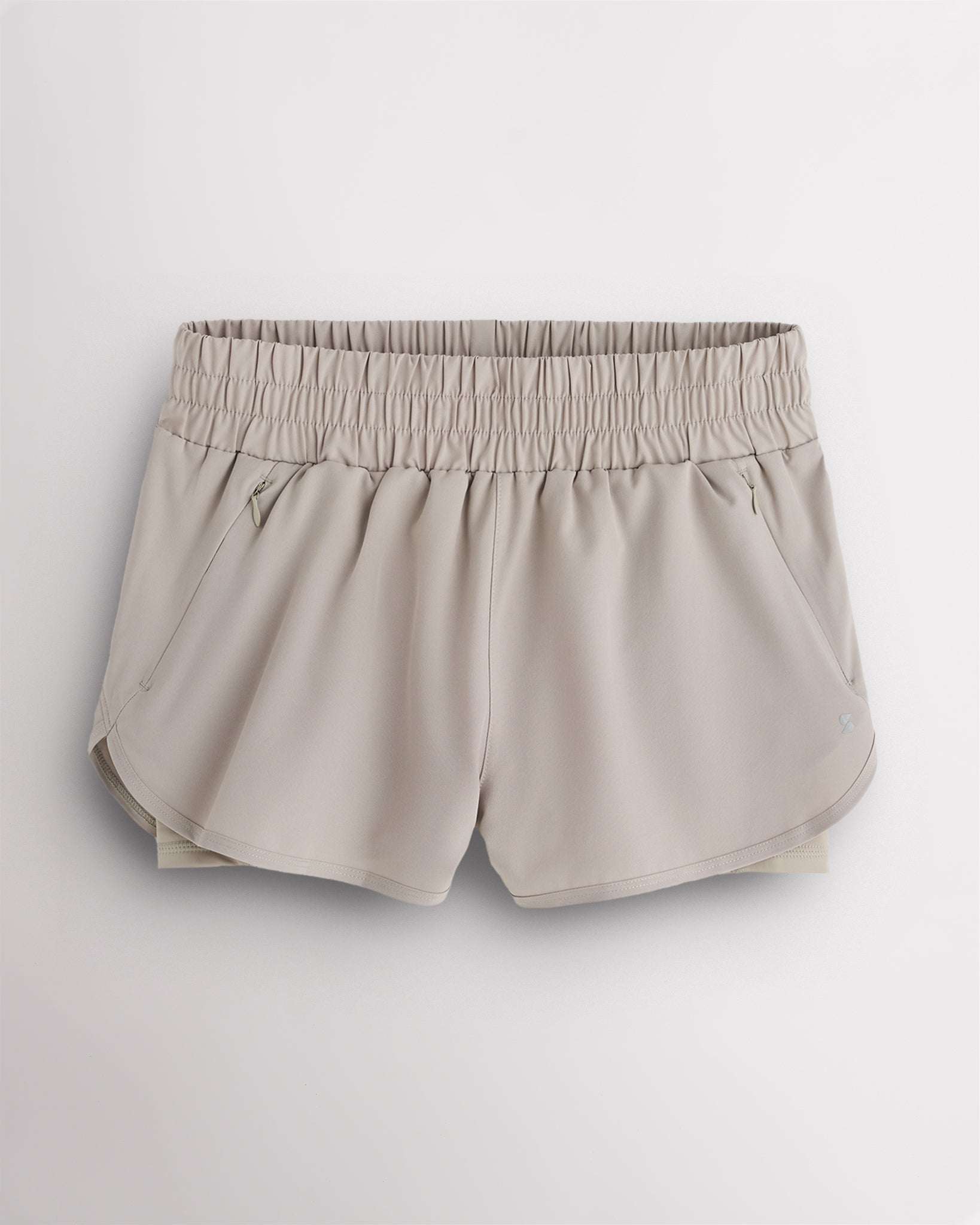 Sandy Grey Stelle RushMode 2-in-1 running shorts with wide elastic waistband, zipper pockets, inner shorts lining, and curved dolphin hem.