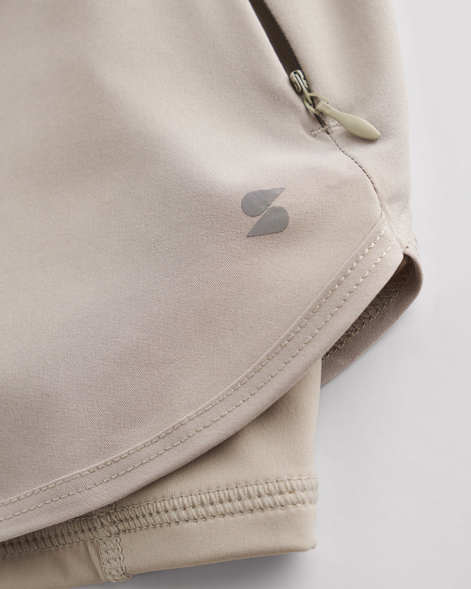 Close-up of Sandy Grey Stelle gym shorts showing zipper pocket, curved hem stitching, and smooth performance fabric.