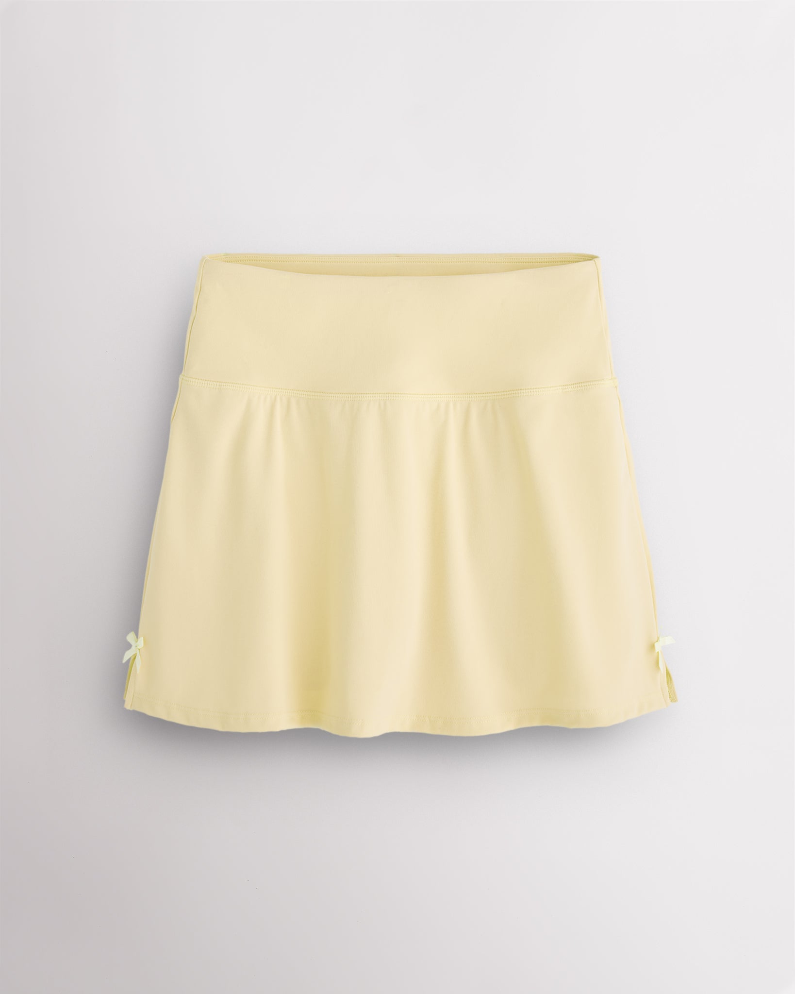 Lemon Butter Stelle classic tennis skirt with a high-waisted fit, slightly flared silhouette, side slits, and bow ribbon details.