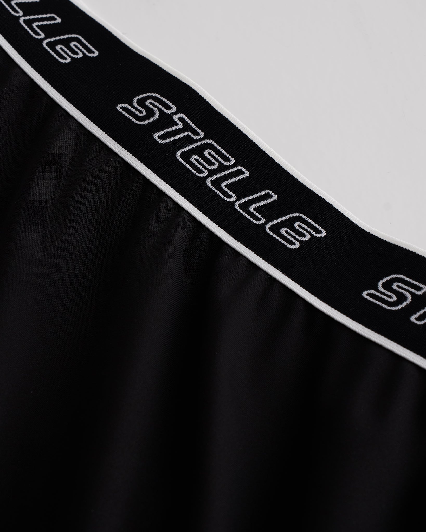 Close-up of black Stelle tennis skirt showing black logo elastic waistband and soft flared fabric detail.