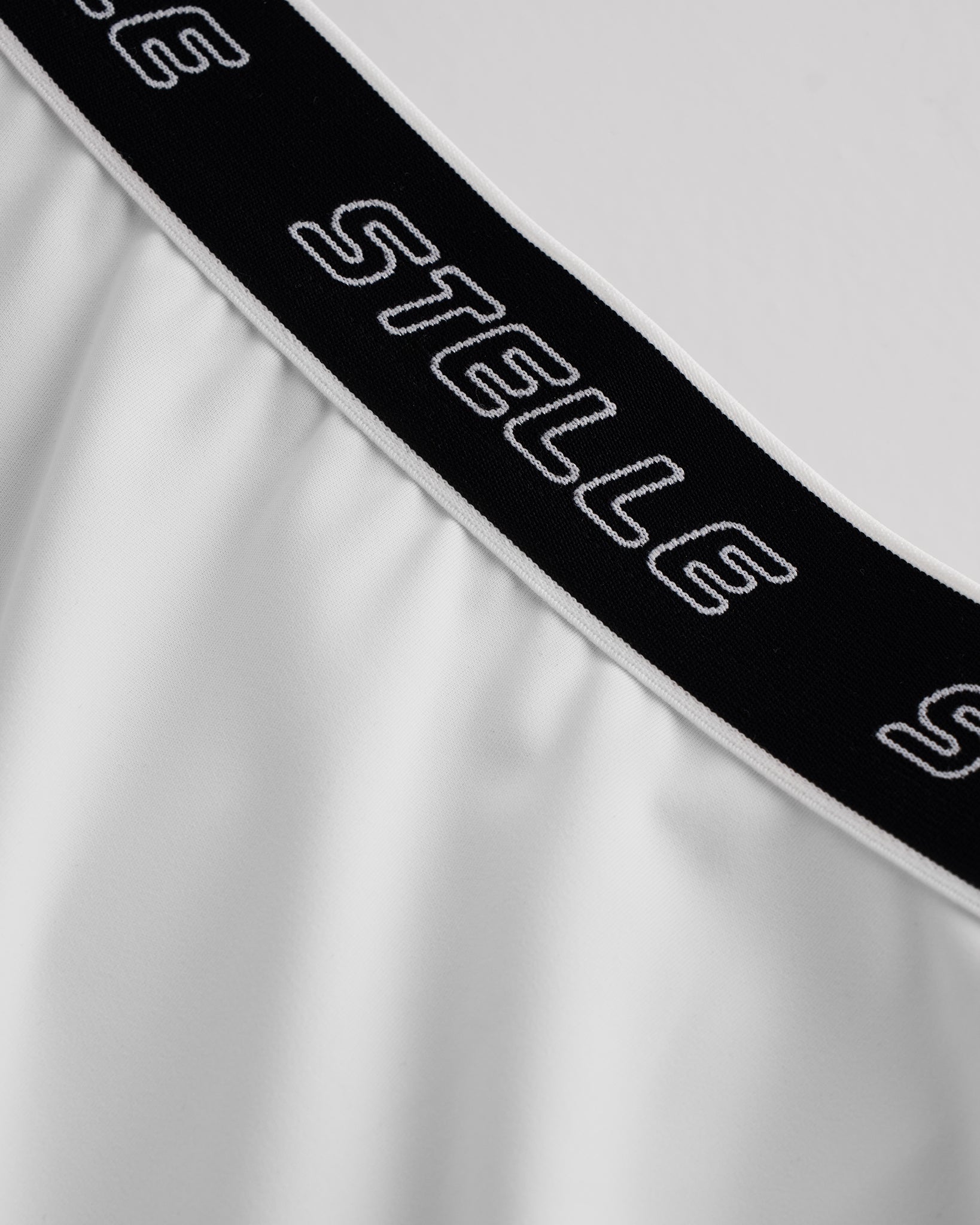 Close-up of white Stelle tennis skirt showing black logo elastic waistband and soft flared fabric detail.