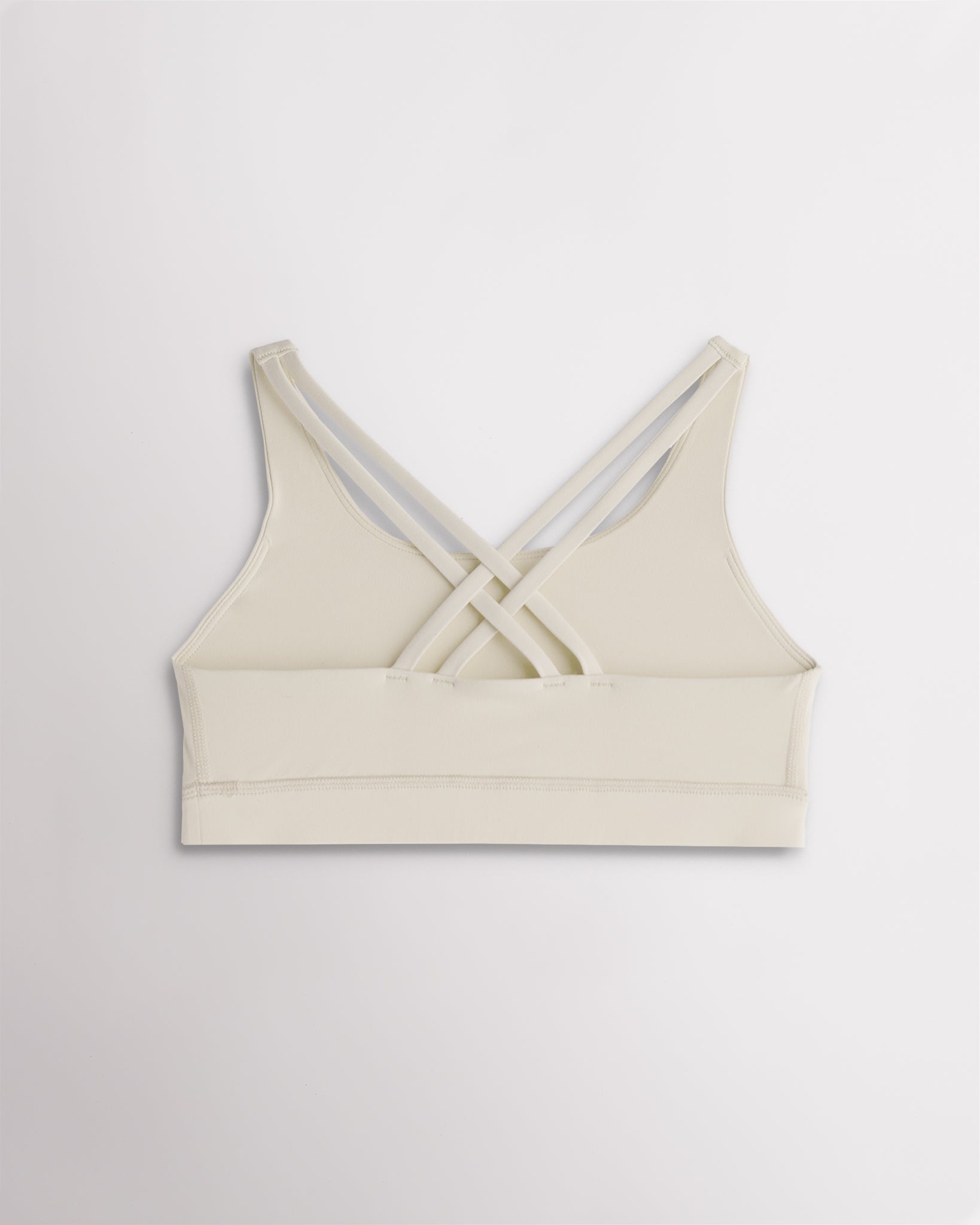Back view of a girls creme sports bra featuring multiple criss-cross straps and a wide supportive band.