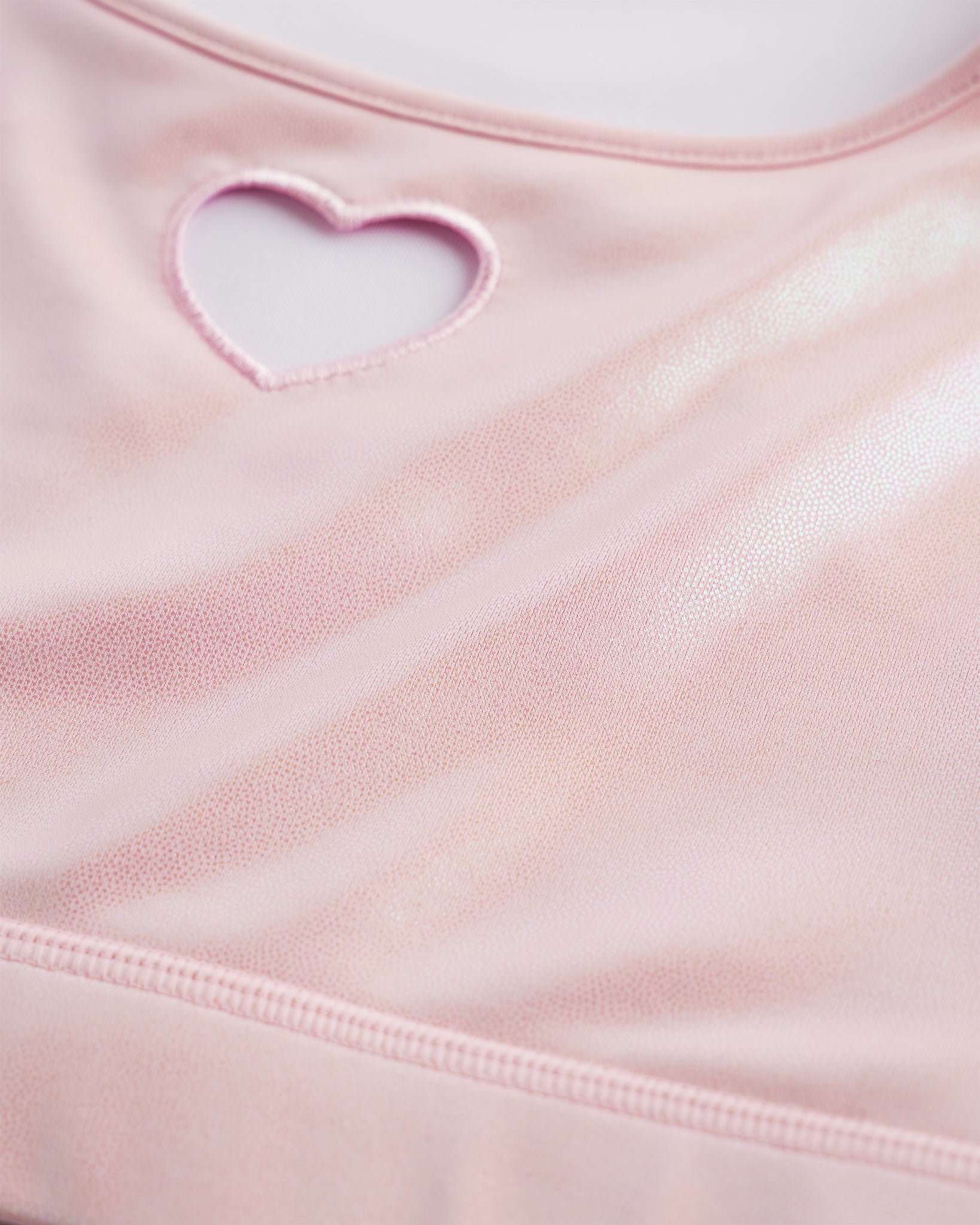 Close-up of pink shimmer crop top showing heart cutout detail, smooth stitching, and iridescent fabric.